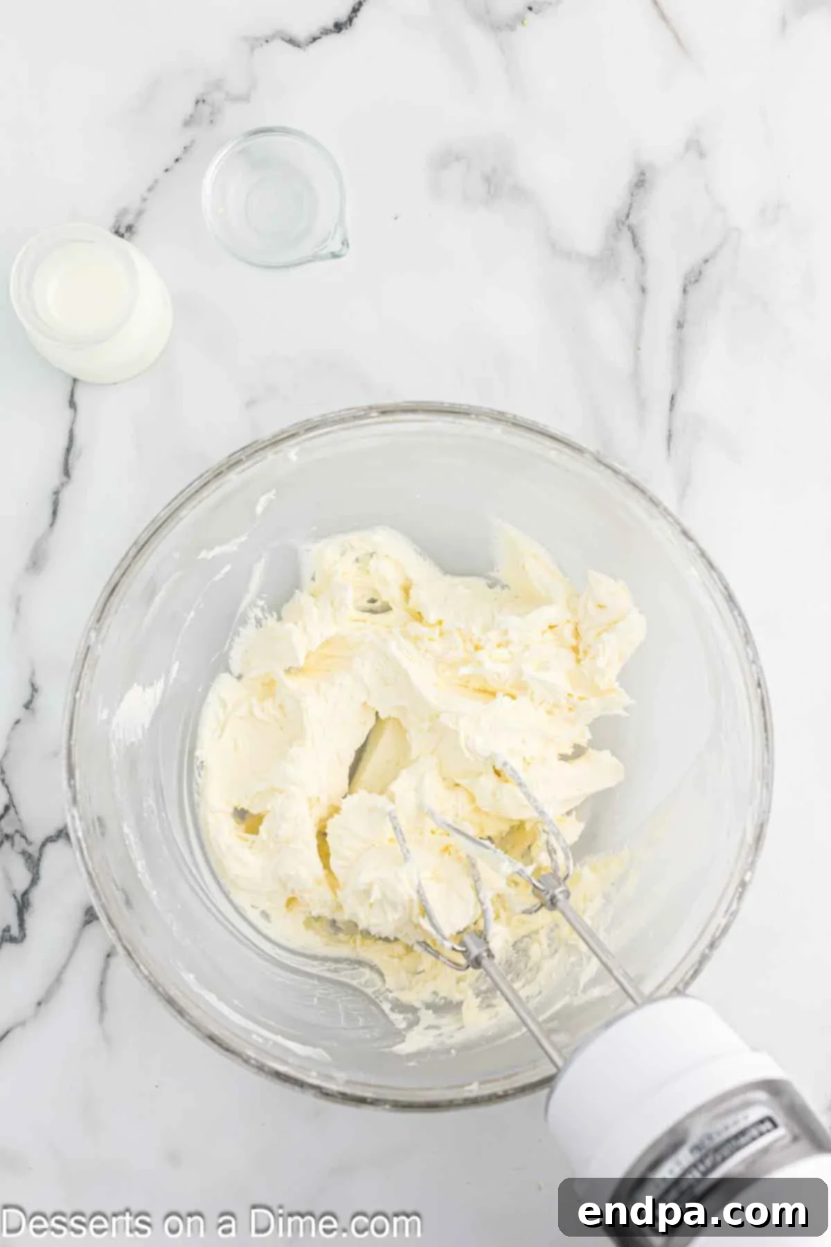Softened butter and powdered sugar being creamed together in a large mixing bowl with a hand-held mixer to create the base for the Spider Web Cupcake frosting.