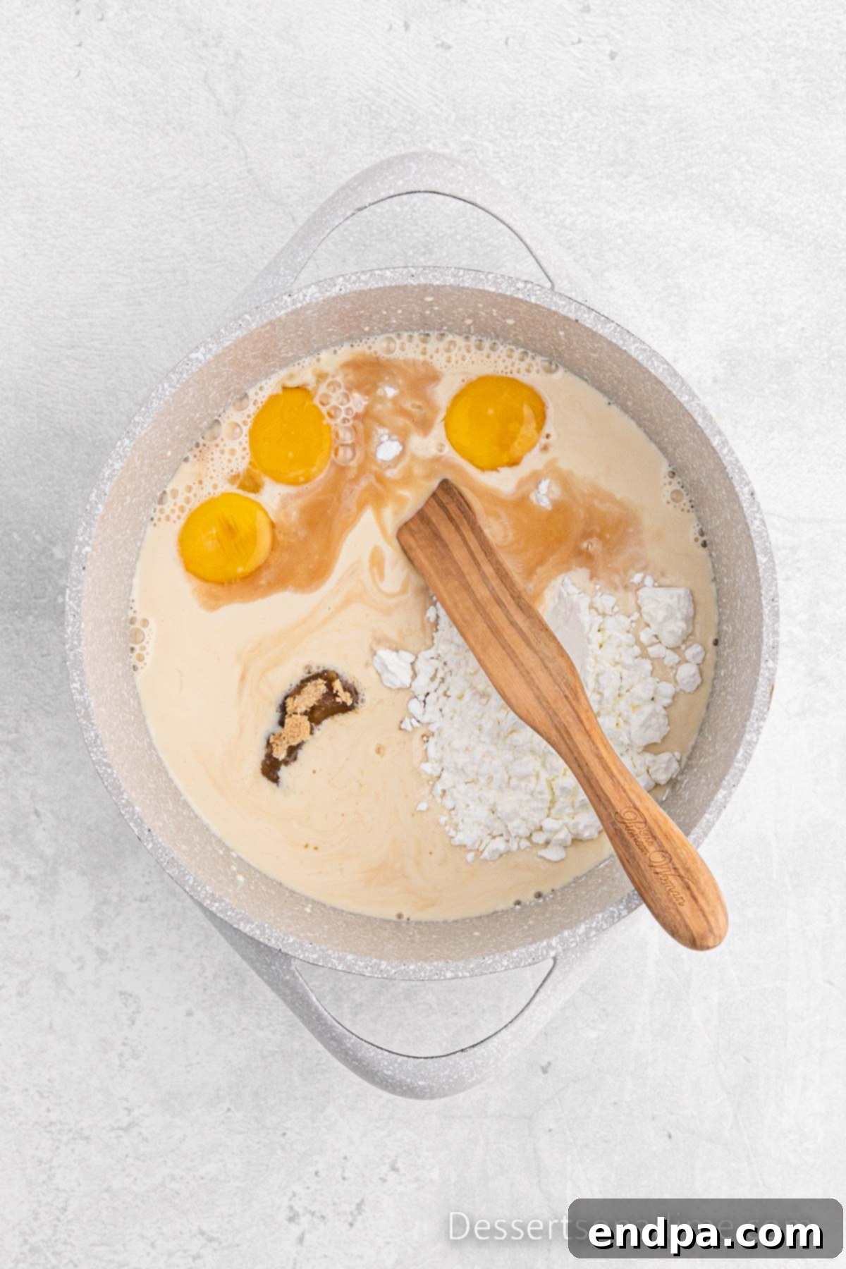 Golden Butterscotch Delight 4 In a large, heavy-bottomed saucepan, the ingredients for the butterscotch pie filling—evaporated milk, brown sugar, cornstarch, egg yolks, vanilla extract, and salt—are being vigorously stirred together with a whisk over medium-high heat on a stovetop, ensuring no lumps form.