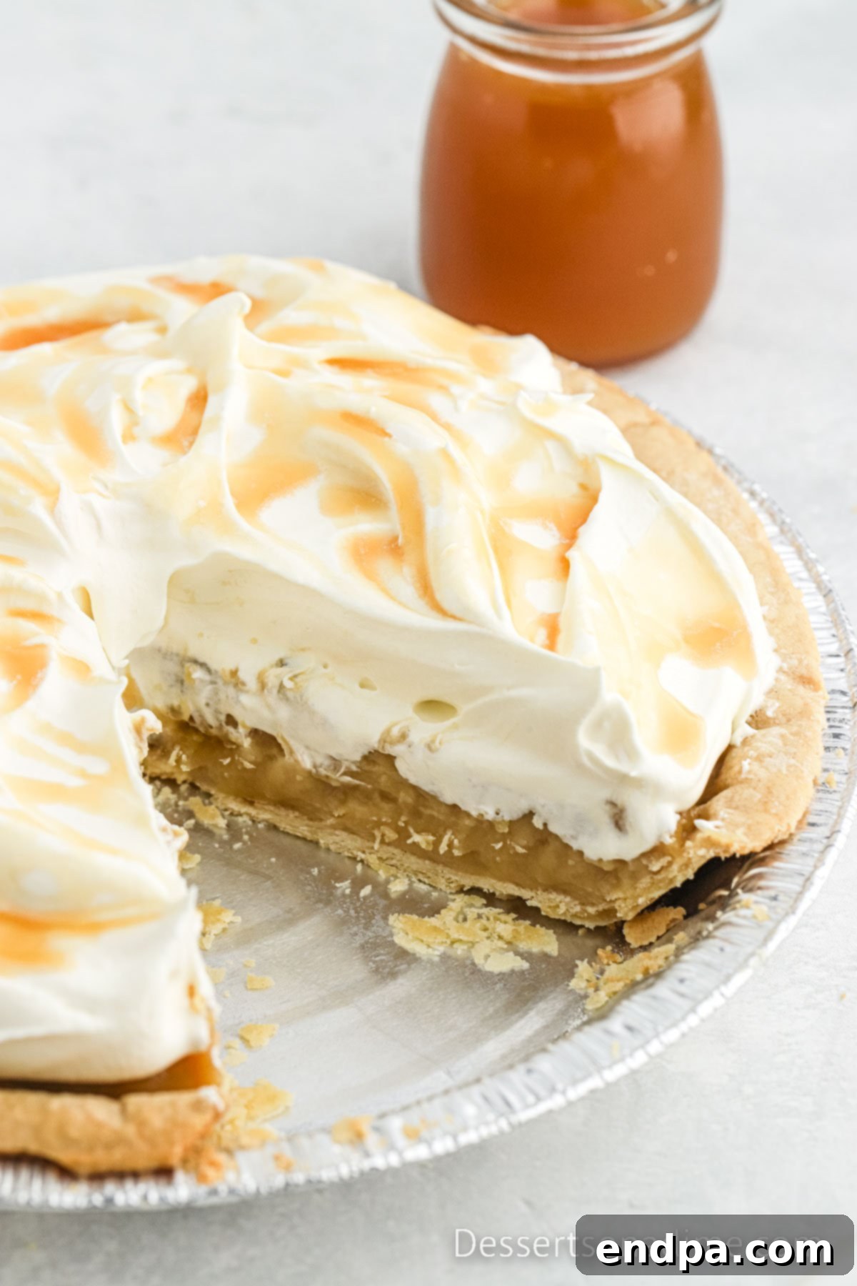 Golden Butterscotch Delight 7 A perfectly set Butterscotch Pie, with a pristine slice carefully removed, revealing its creamy, golden filling and flaky crust inside a classic pie pan. The remaining pie is ready to be garnished with whipped cream and butterscotch syrup before serving.