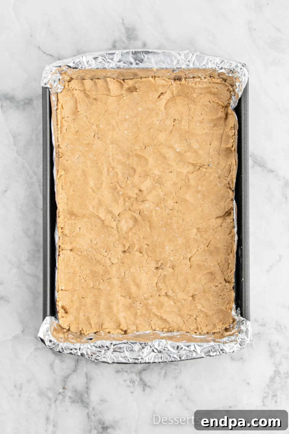 The peanut butter mixture has been pressed evenly into the bottom of the prepared 9x13 inch baking pan.