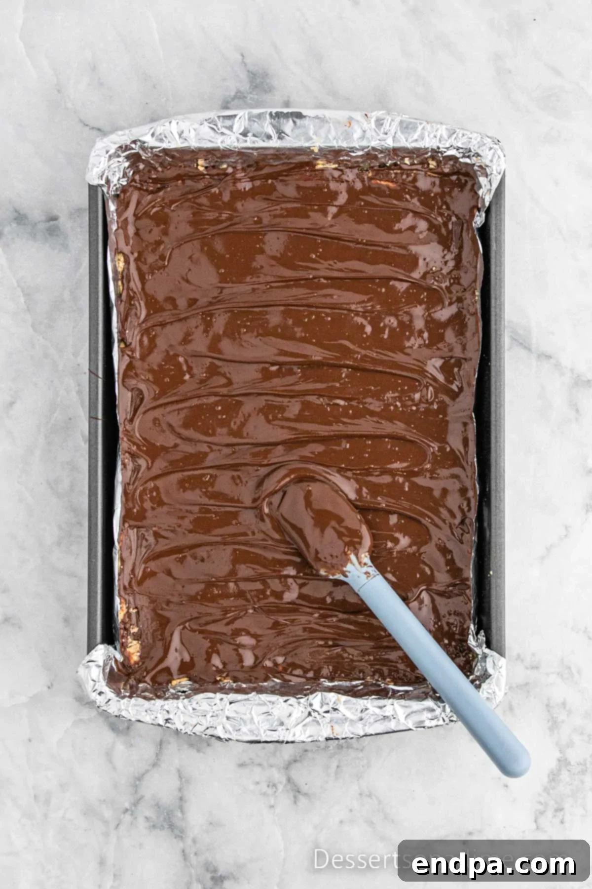 Melted chocolate and shortening are spread smoothly over the peanut butter layer with a spatula.