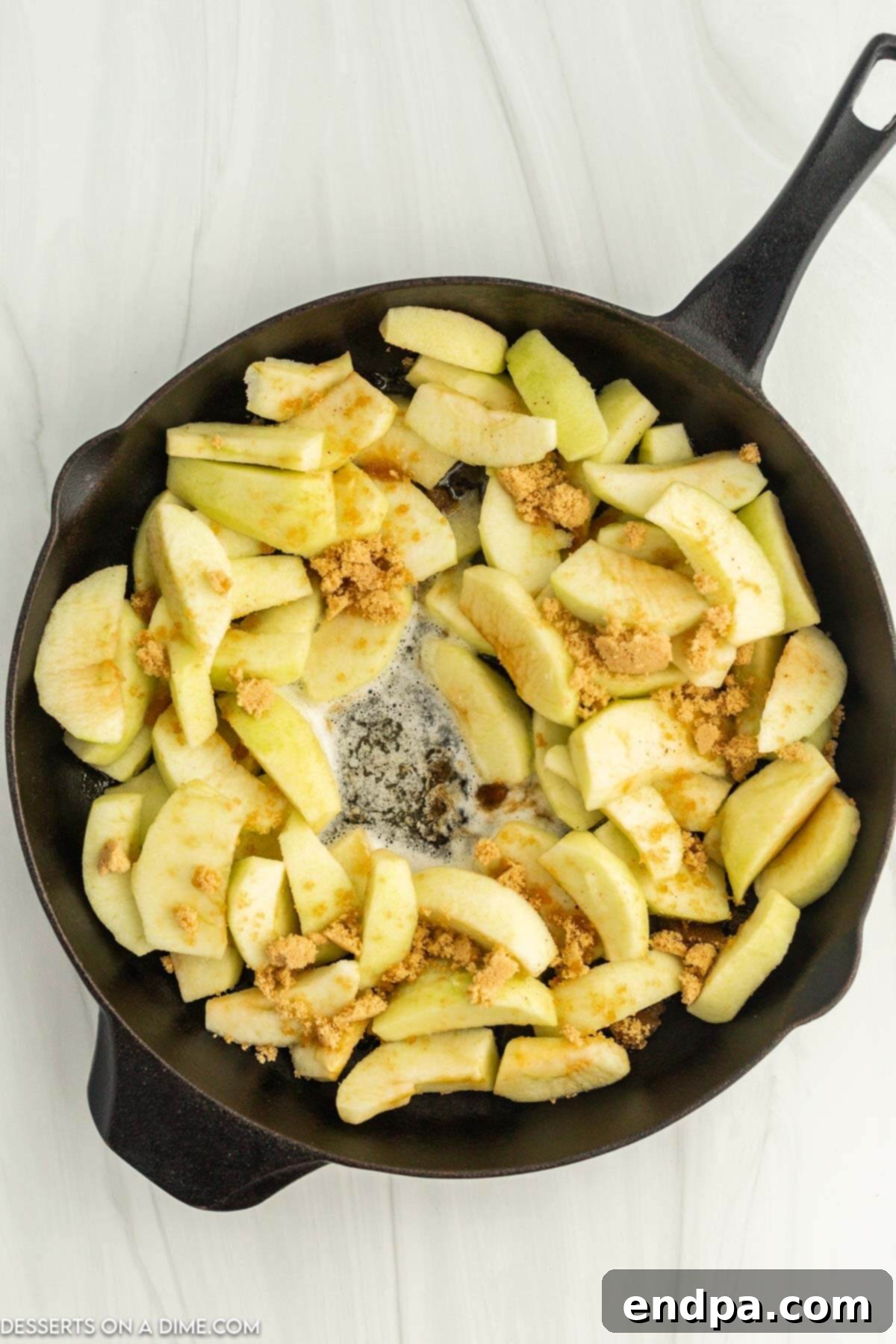 Apple slices simmering in a cast iron skillet with melted butter, brown sugar, and cinnamon, creating a rich caramel sauce.