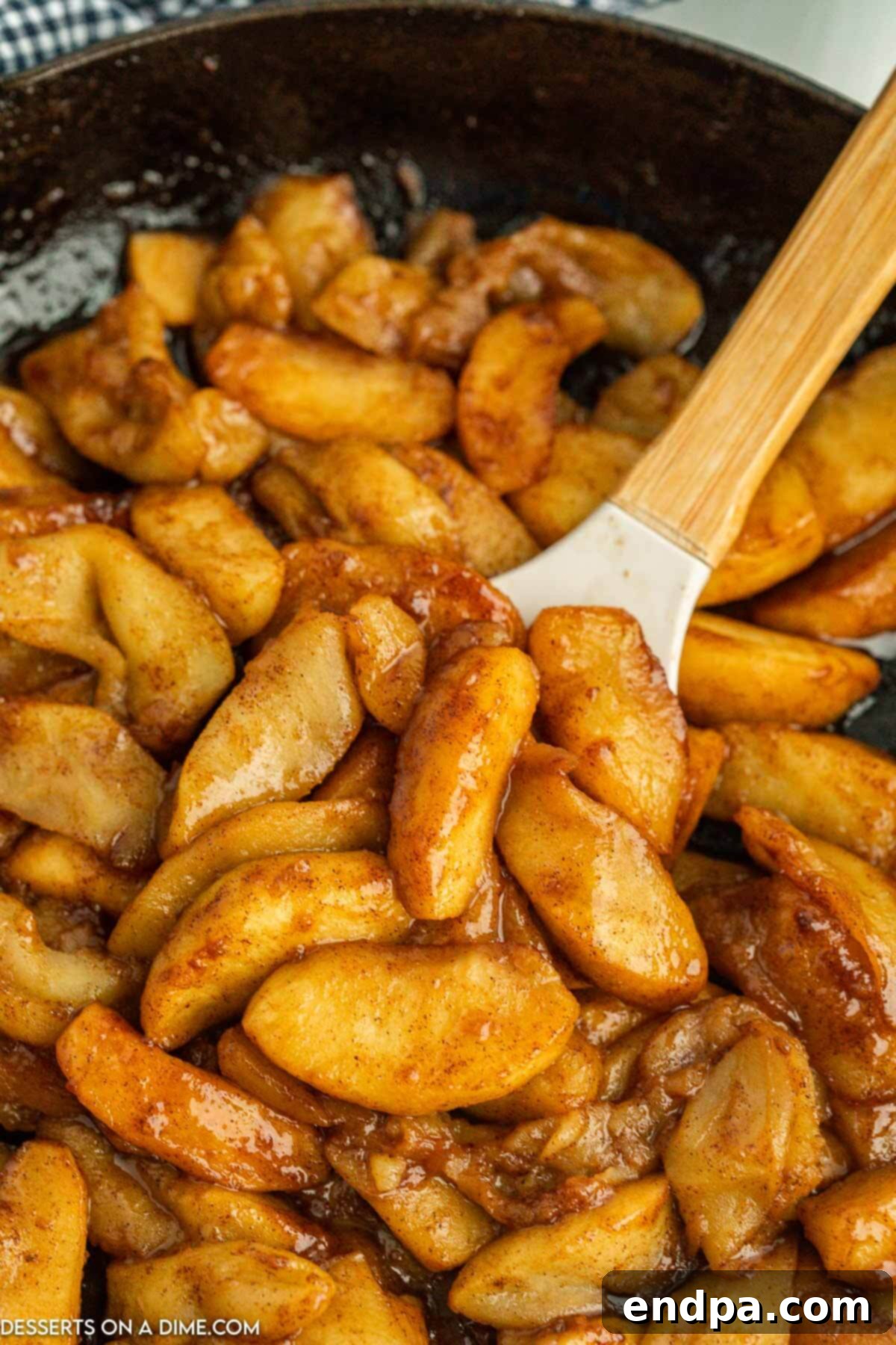 Tender fried apples being gently stirred in a skillet, coated in a luscious brown sugar and cinnamon glaze.