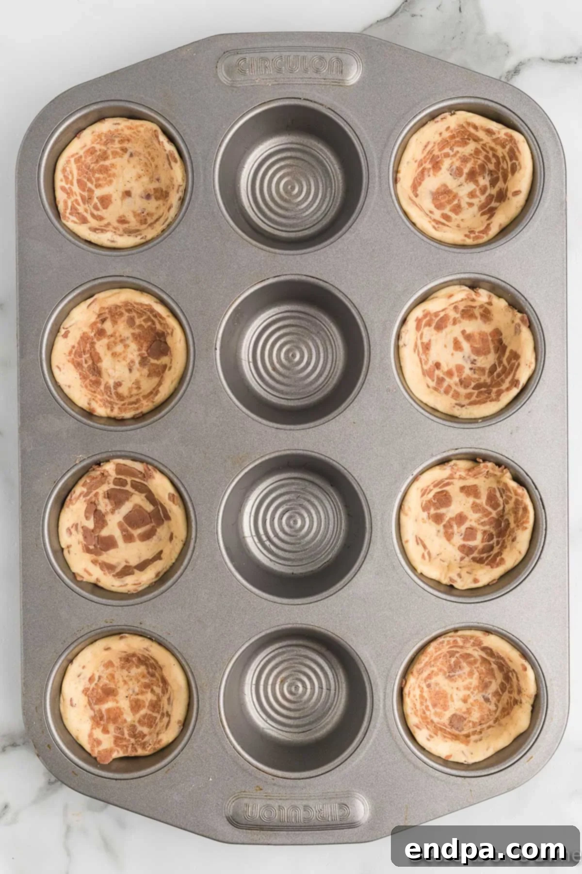 Flattened cinnamon rolls carefully placed into a muffin tin, forming the cups.