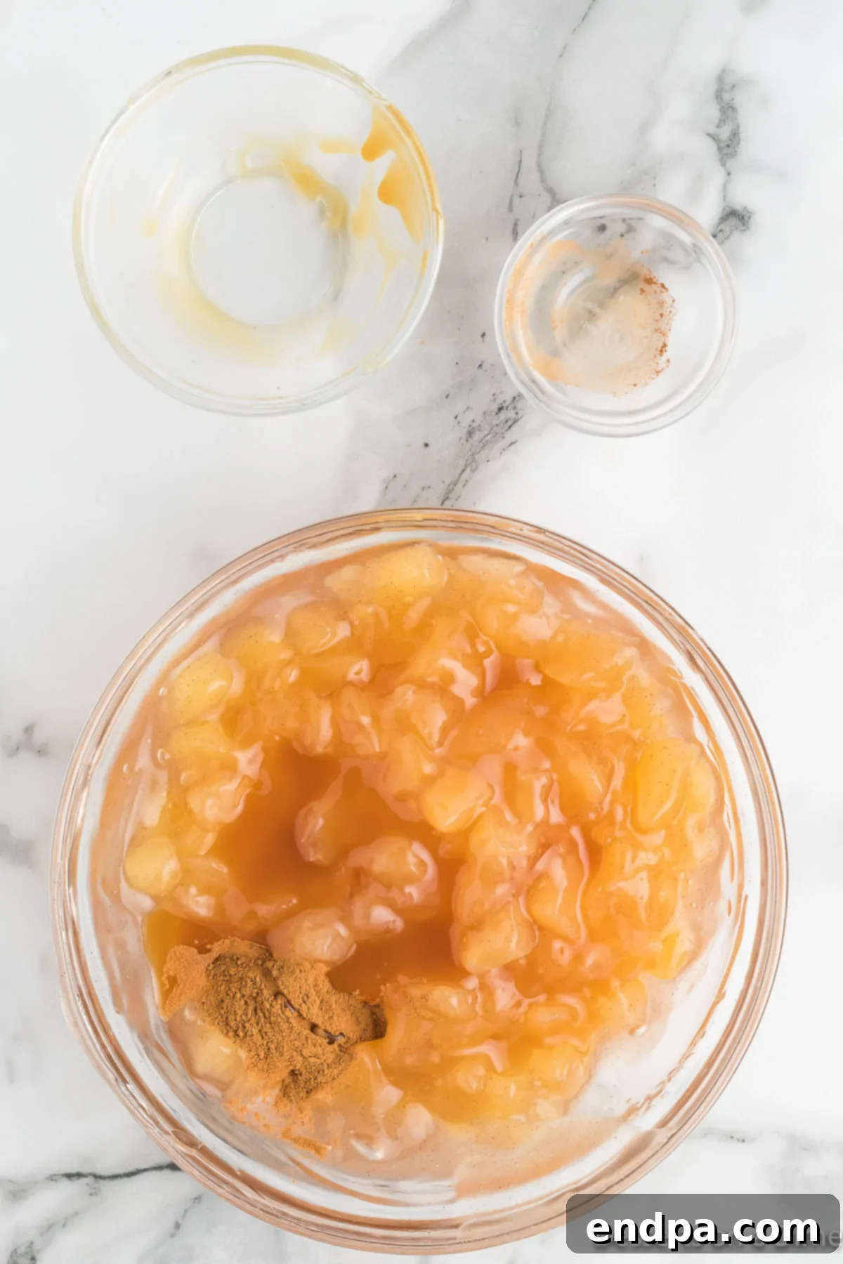 Caramel sauce being stirred into the apple pie filling mixture in a bowl.