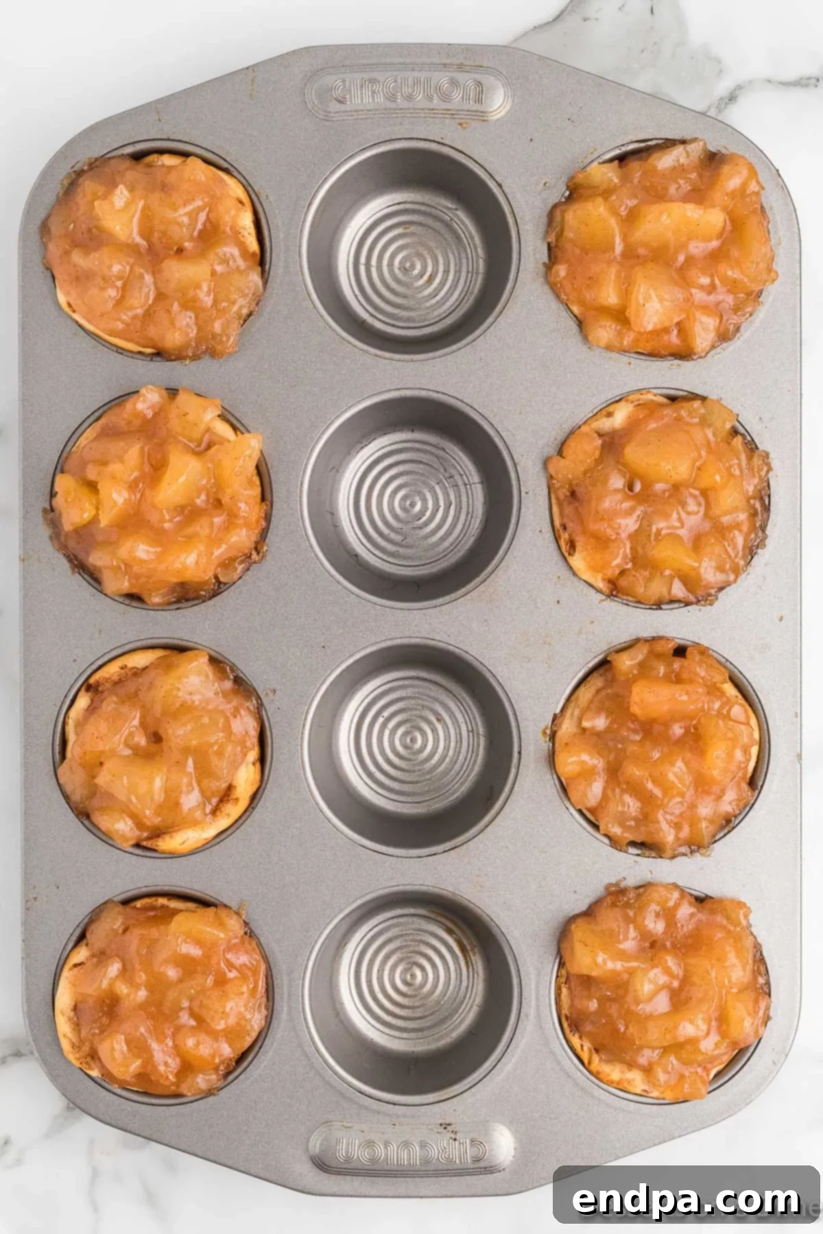 Apple pie filling generously placed into each cinnamon roll cup in the muffin tin.
