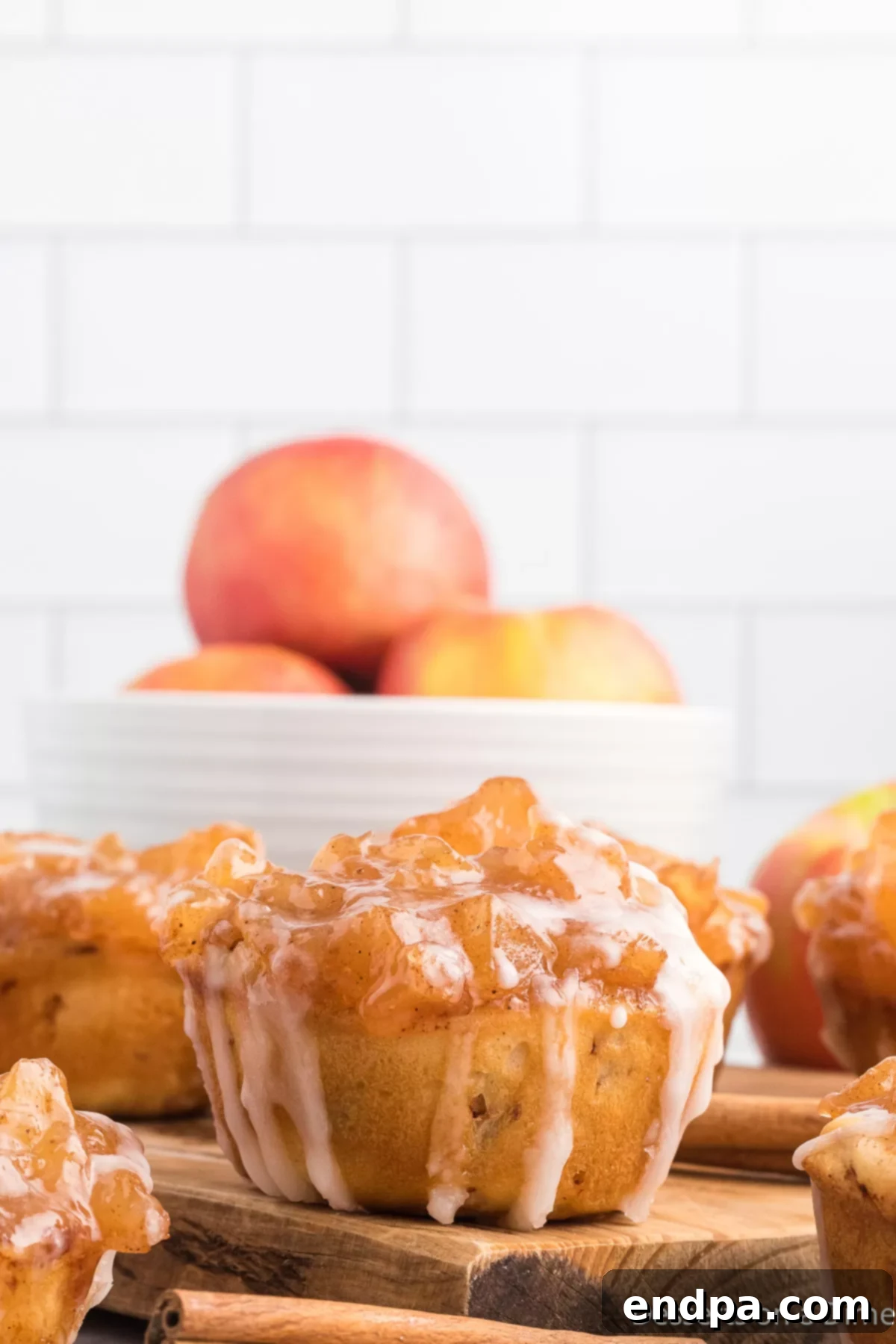 A collection of freshly baked Cinnamon Roll Apple Pie Cups arranged on a wooden cutting board, glistening with glaze.