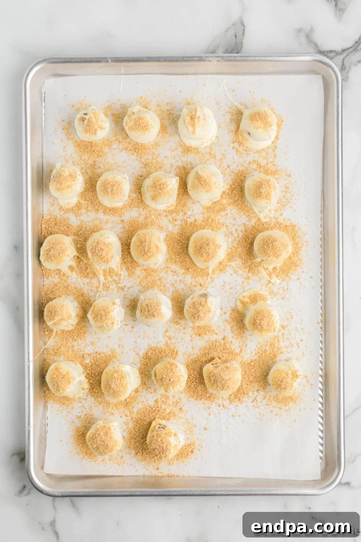 Finished pumpkin truffles on a baking sheet, freshly coated and topped with graham cracker crumbs.