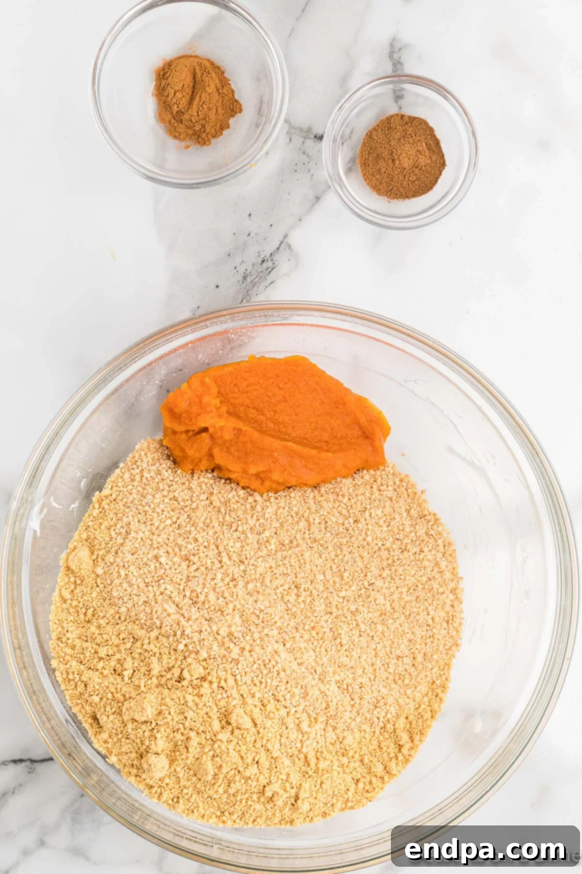 A bowl containing pumpkin puree, graham cracker crumbs, and spices, ready for mixing.