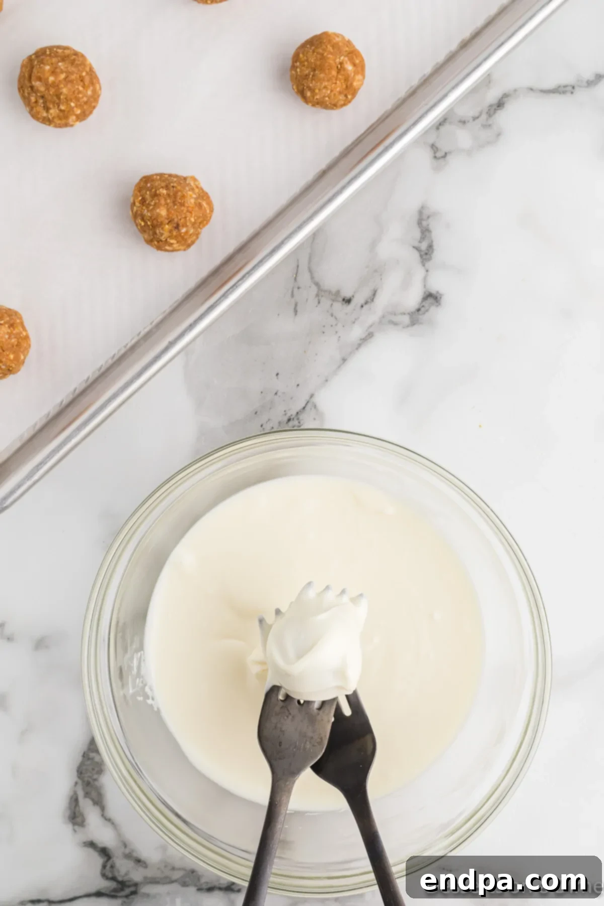 Pumpkin truffle balls being dipped into melted white chocolate using two forks.