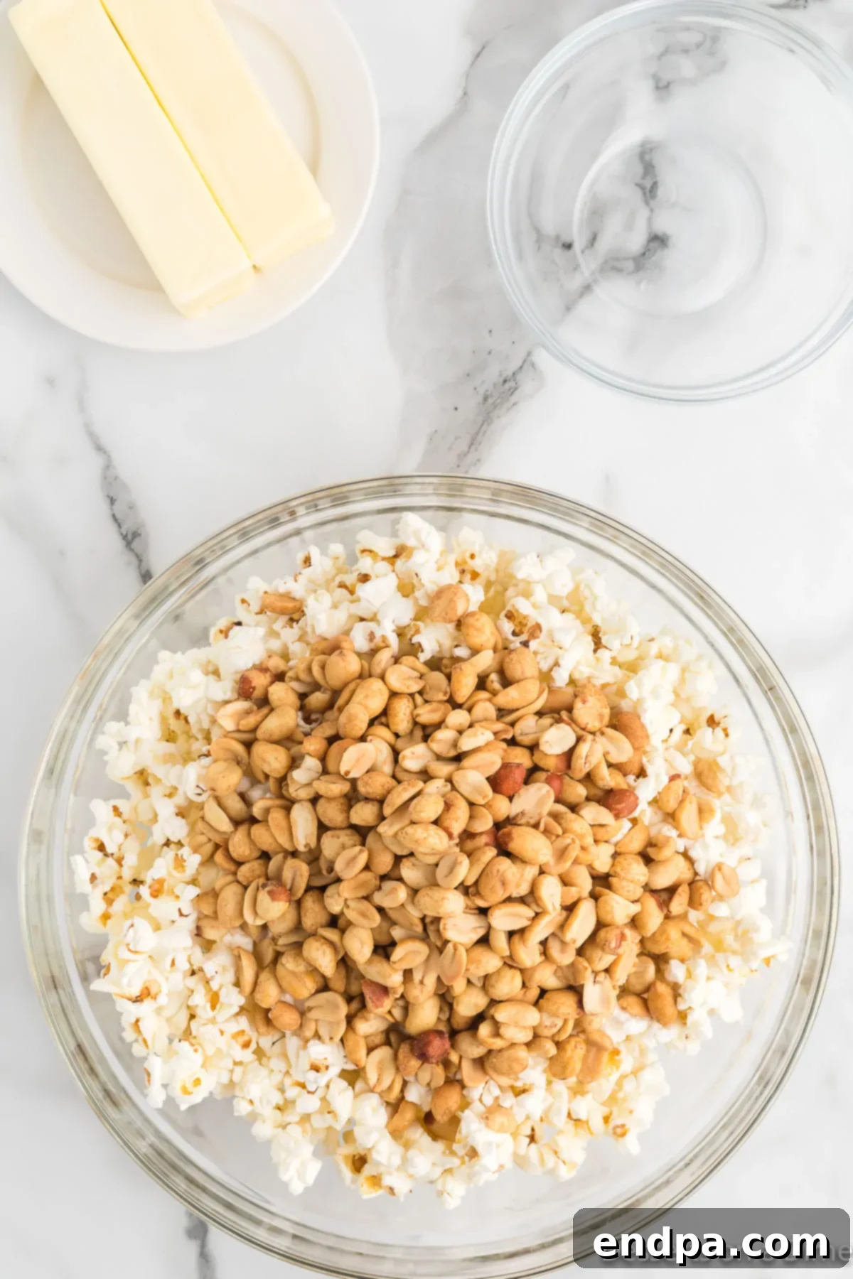 Adding roasted peanuts to a bowl of popped popcorn, preparing for the toffee coating.