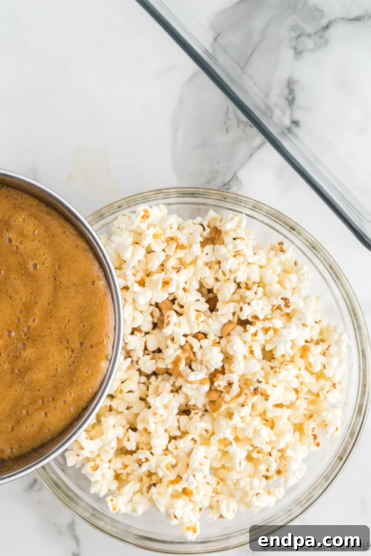 Pouring the warm, golden toffee mixture over the popcorn in a large bowl, ready for coating.
