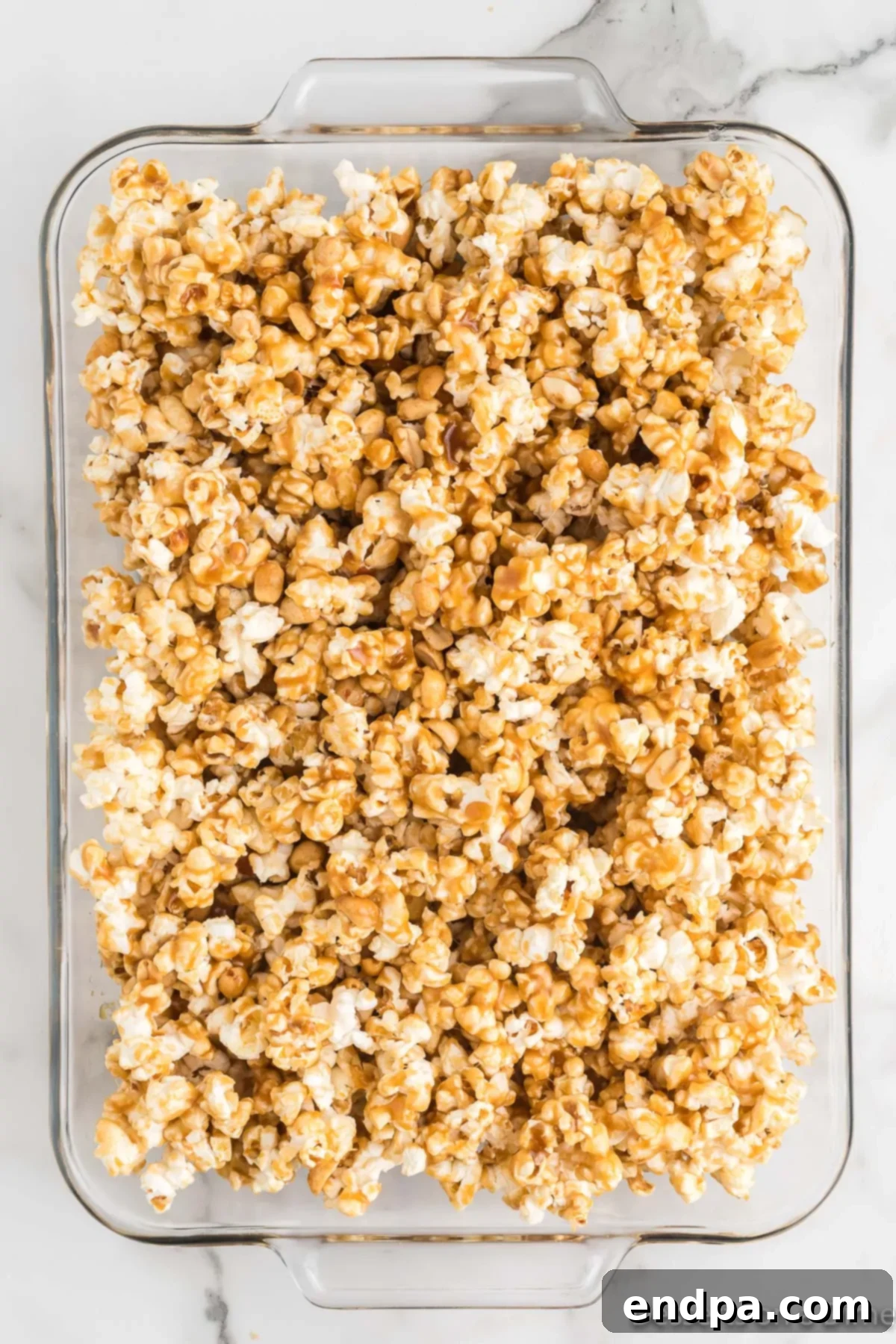 Spreading the coated butter toffee popcorn onto a baking sheet lined with parchment paper.