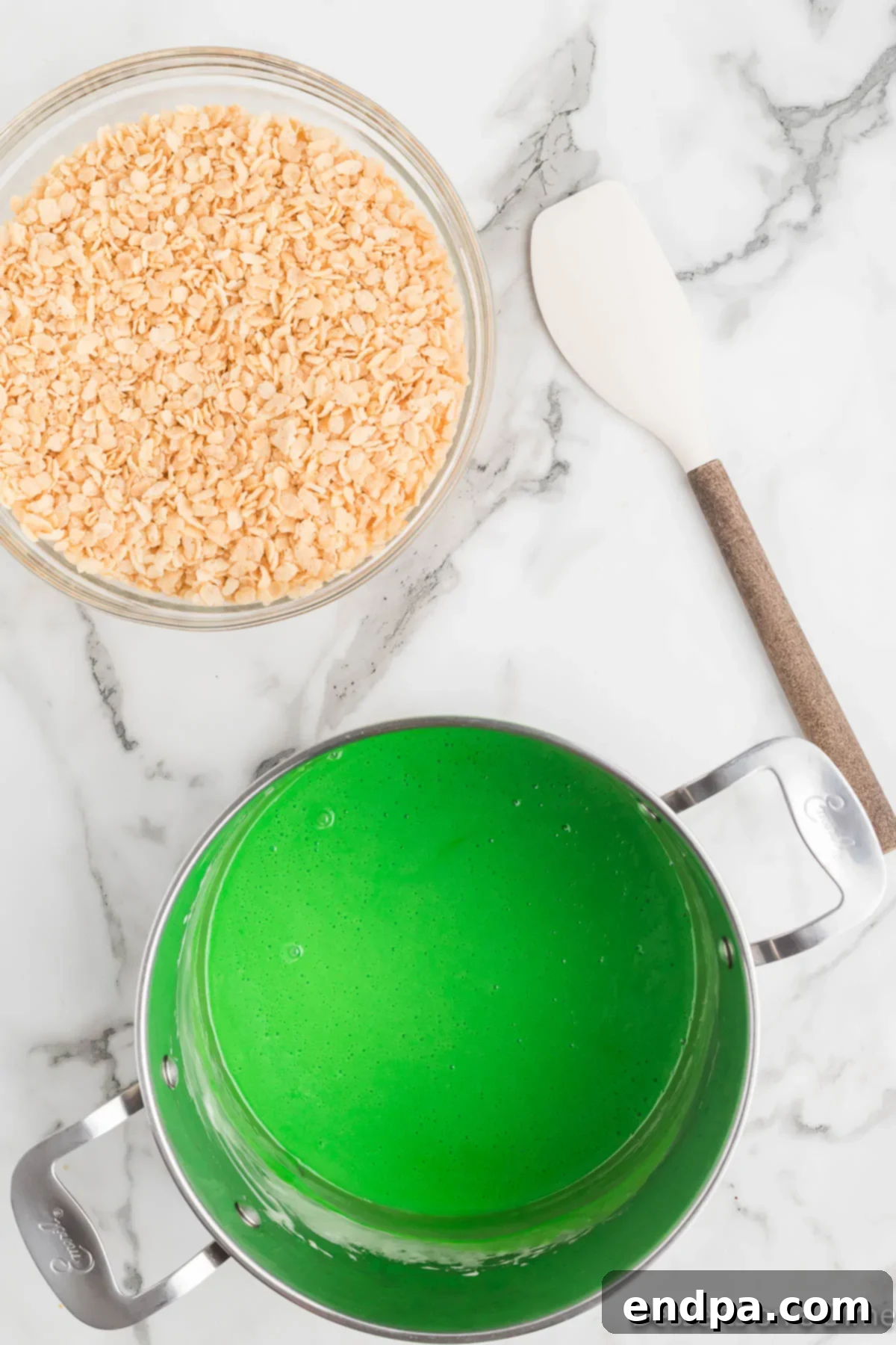 Vibrant green food coloring being mixed into the melted marshmallow mixture.