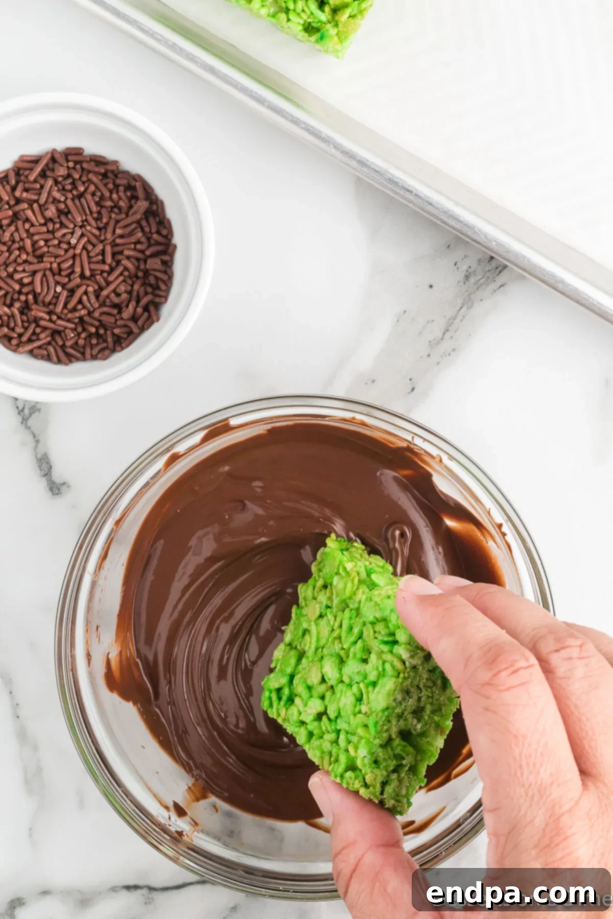 Cooled green Rice Krispie treats being dipped into melted chocolate for Frankenstein's hair.