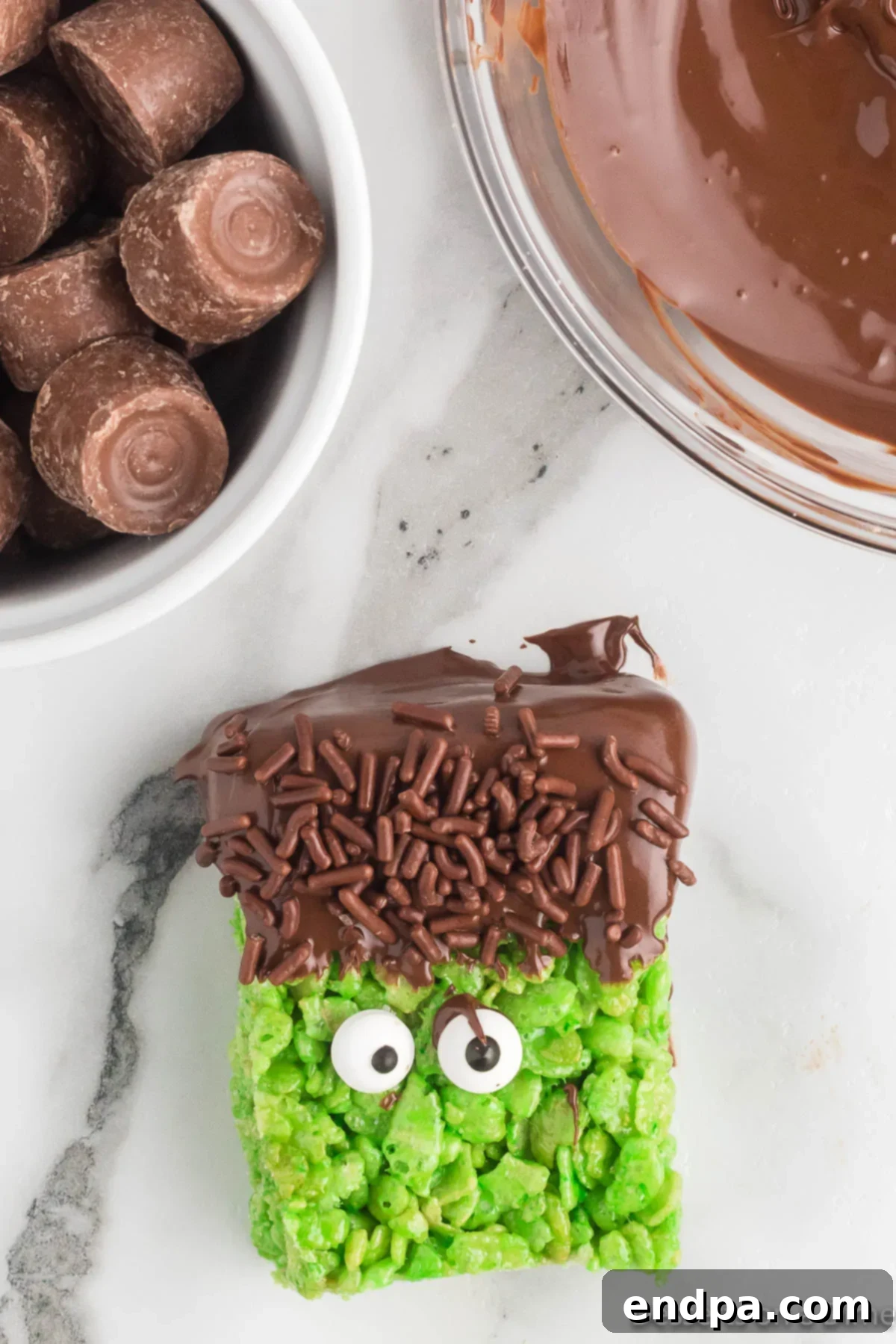 Frankenstein Rice Krispie treats with chocolate hair, sprinkles, and candy eyes, ready for facial details.