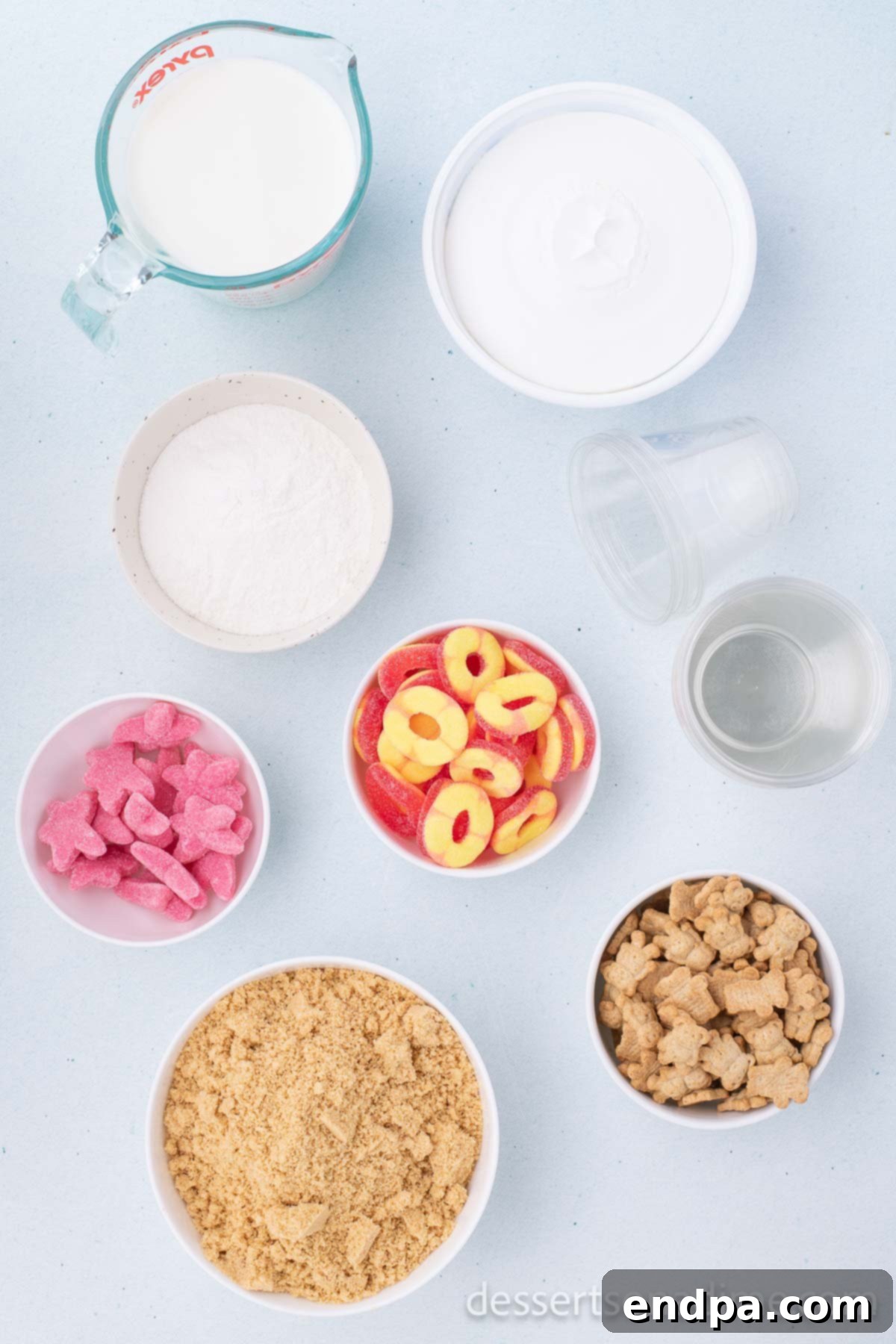 Ingredients for Sand Pudding Cups laid out: instant vanilla pudding mix, milk, whipped topping, Golden Oreo cookies, and assorted gummy candies.