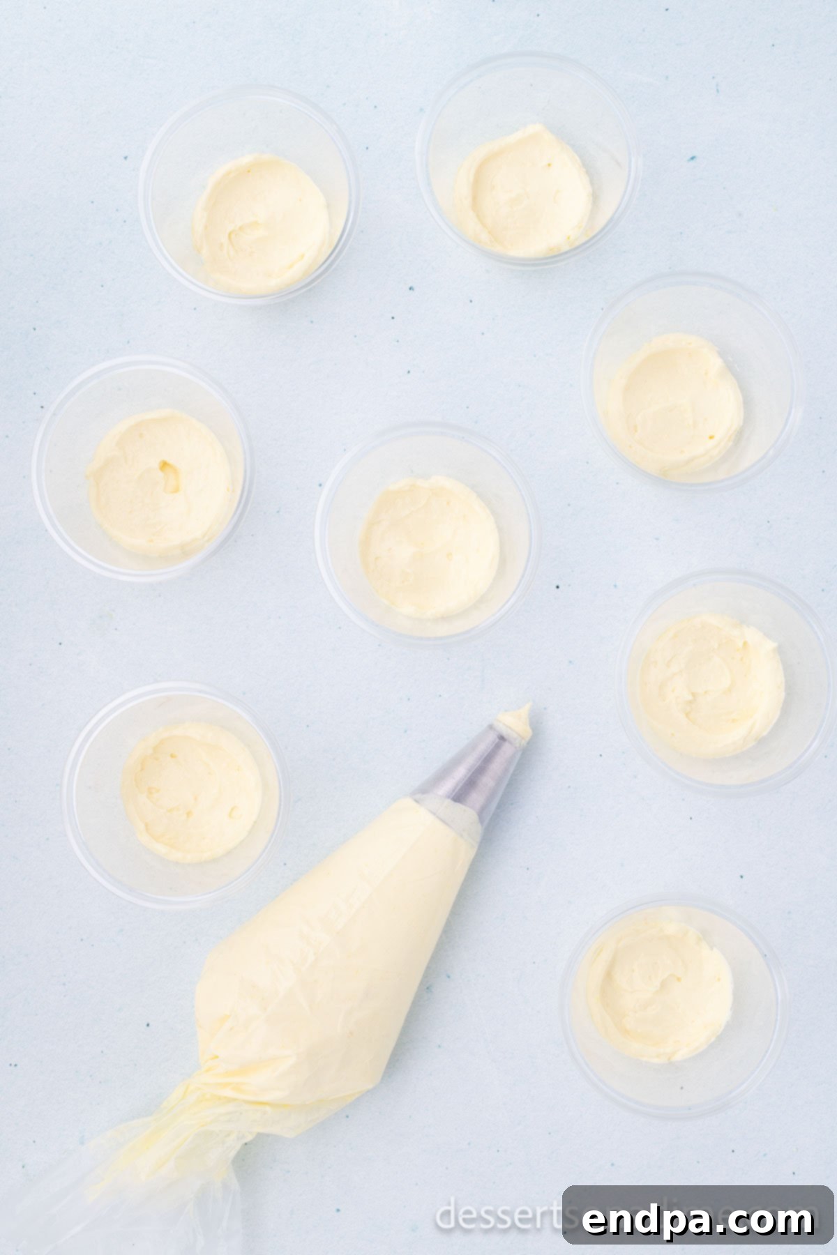 Creamy pudding mixture being piped or spooned into clear plastic cups.
