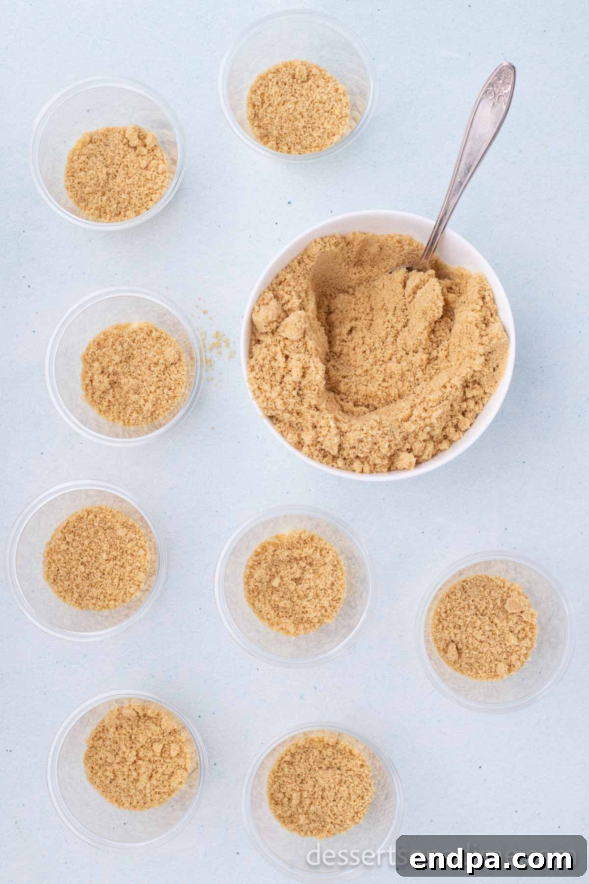 Crushed Golden Oreo cookie crumbs being layered over the pudding in cups to resemble sand.