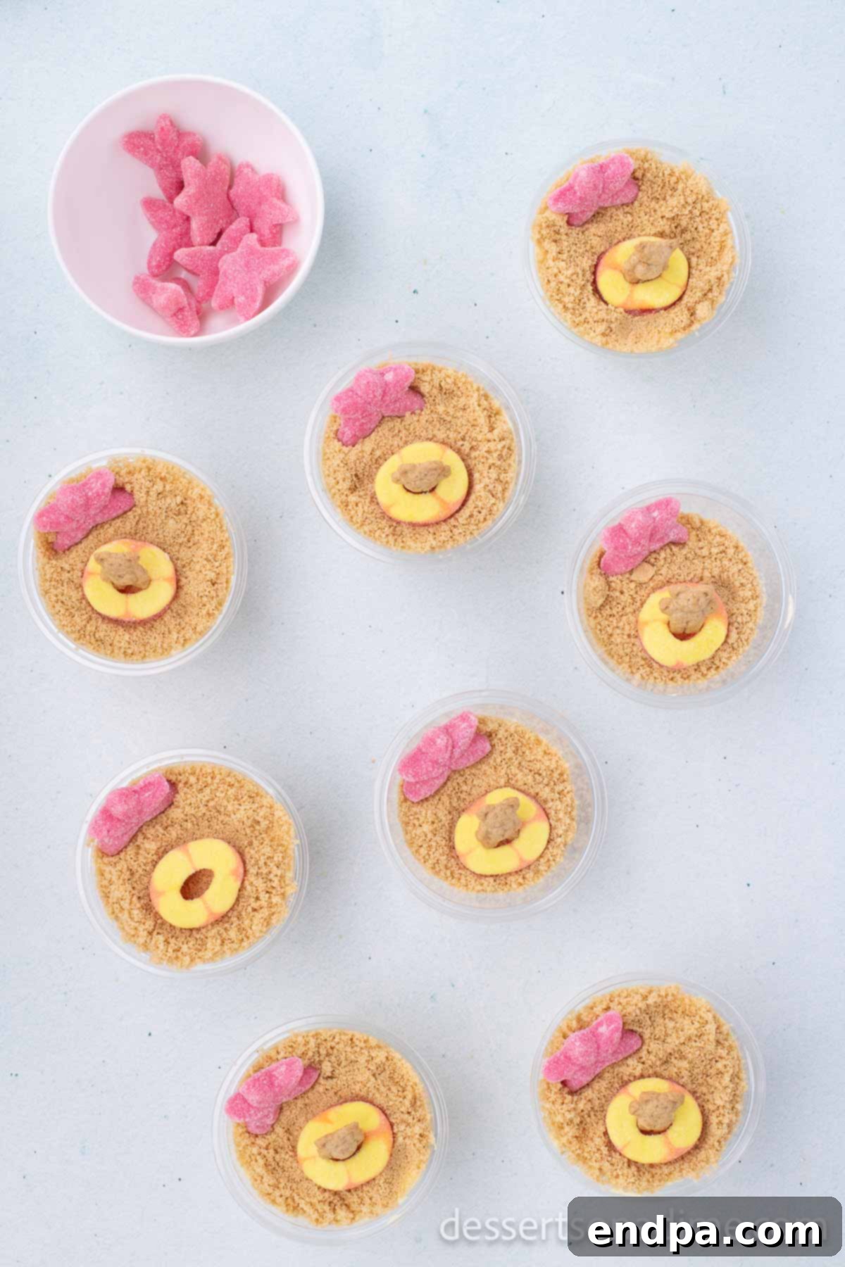 Various candies and a teddy graham arranged on top of the cookie crumbs to create a miniature beach scene, with the teddy graham appearing to float.
