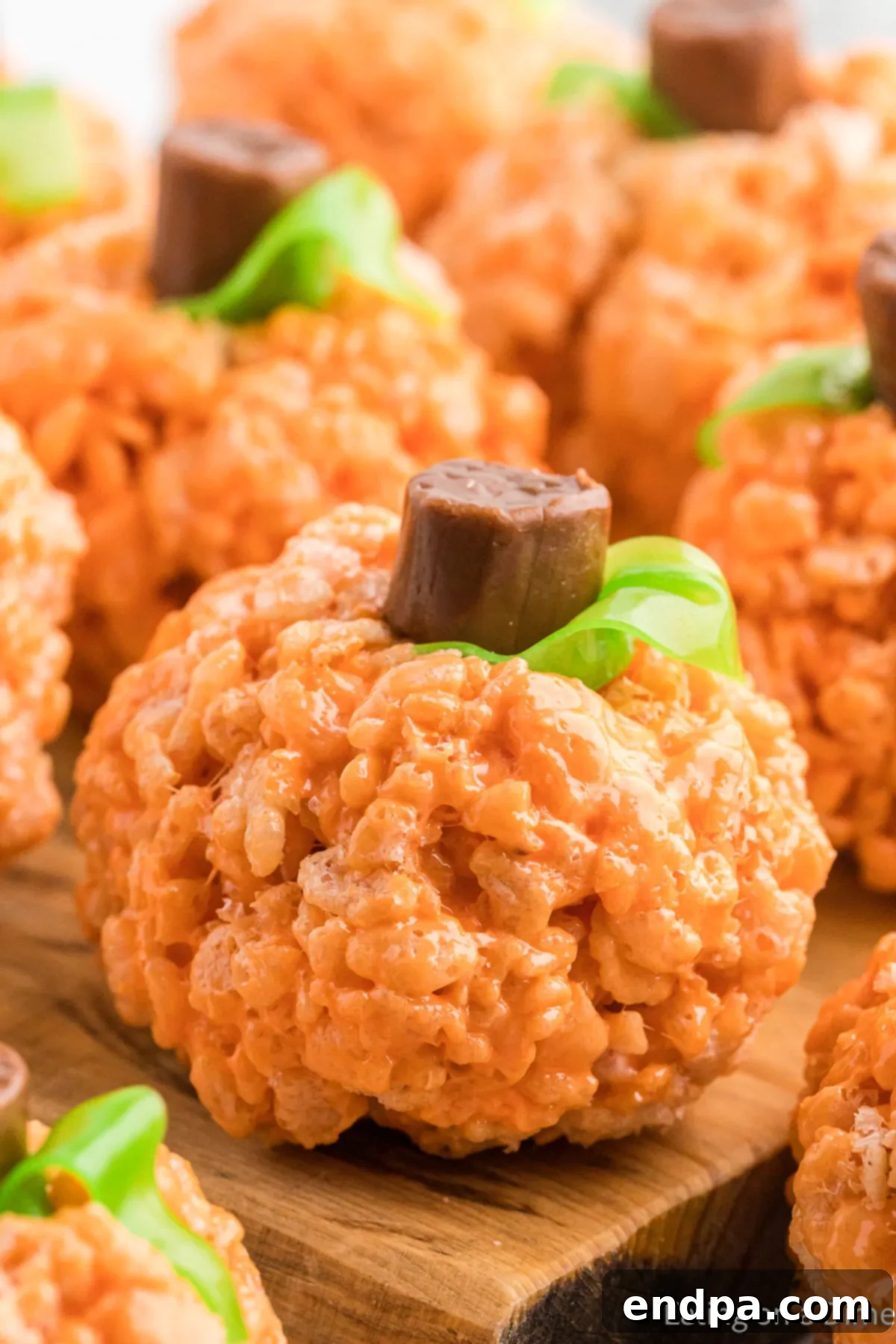 Pumpkin Patch Krispie Treats 2 Adorable Pumpkin Rice Krispie Treats decorated with chocolate stems and green fruit roll-up leaves, arranged artfully on a rustic wooden board.