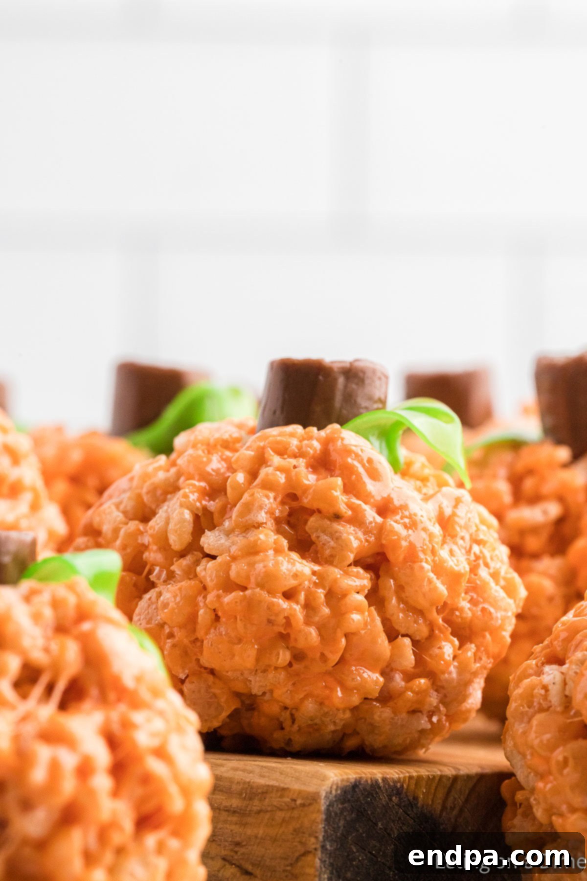 Pumpkin Patch Krispie Treats 3 Close-up of a perfectly formed Pumpkin Rice Krispie Treat, showcasing its bright orange color, chocolate stem, and delicate fruit roll-up vine, sitting on a wooden board.