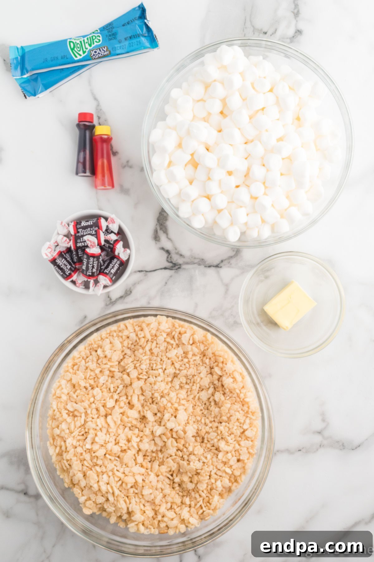 Pumpkin Patch Krispie Treats 4 A flat lay showing the essential ingredients for pumpkin rice krispie treats: a box of Rice Krispies cereal, a stick of butter, a bag of mini marshmallows, a handful of Tootsie Rolls, and green fruit roll-ups.