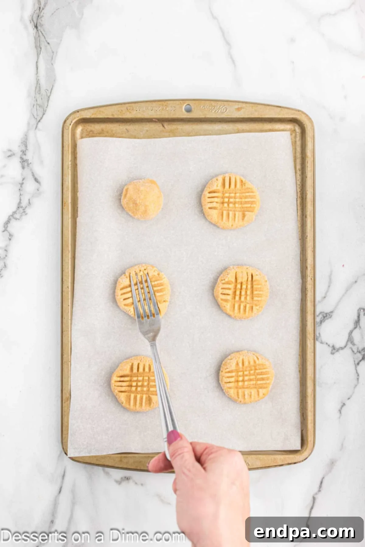 Fork pressed into cookie dough balls creating a criss-cross design before baking.