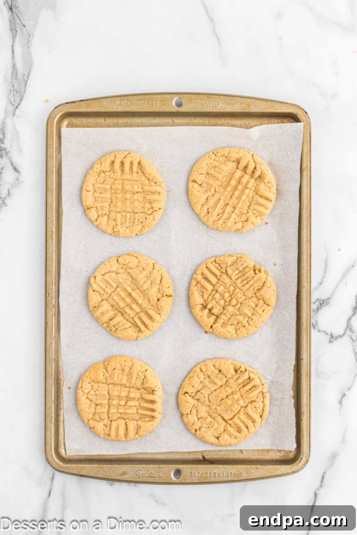 Freshly baked peanut butter cookies cooling on a baking sheet, lightly golden brown.