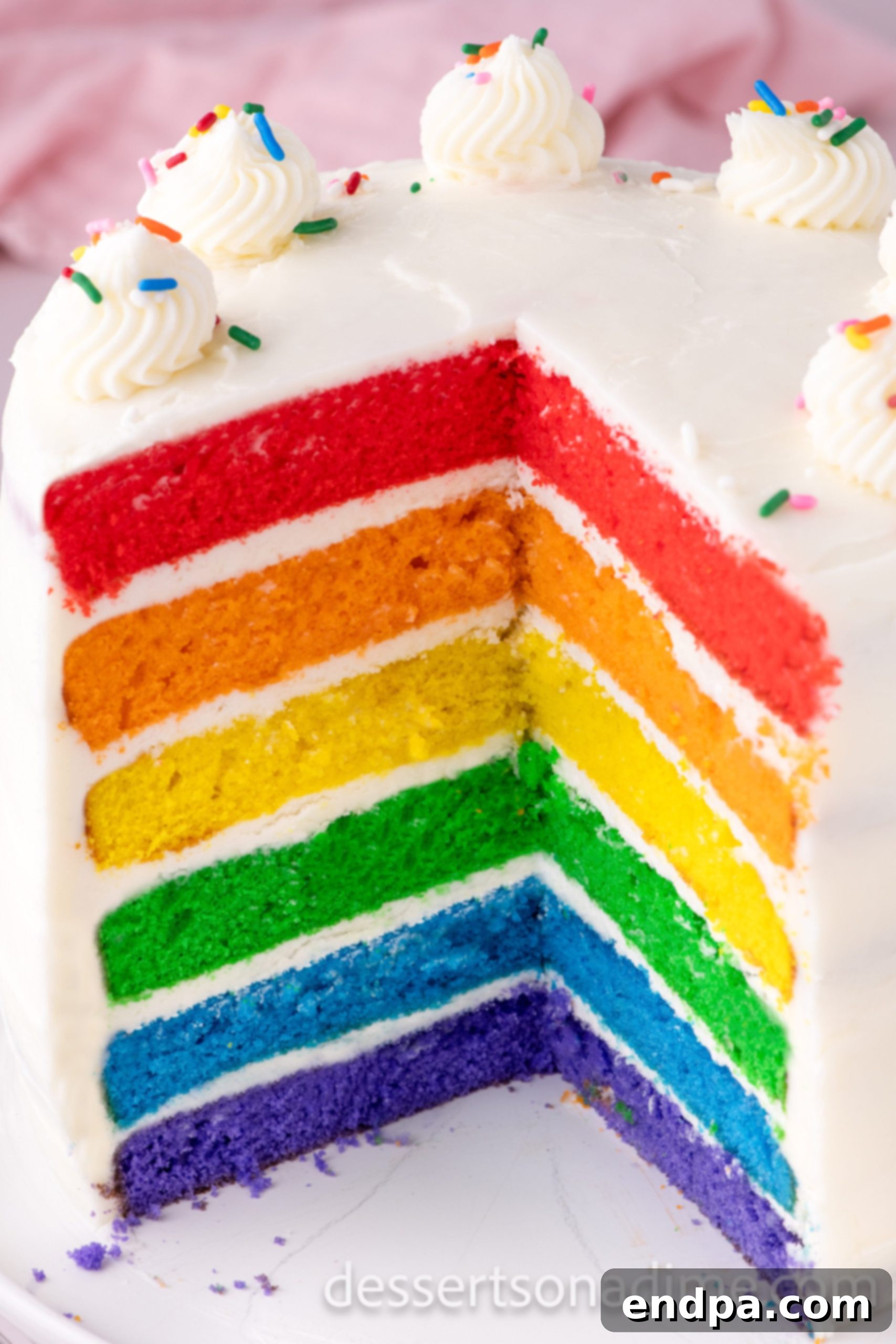 Kaleidoscope Delight 12 A freshly sliced piece of Rainbow Cake, showcasing its perfectly stacked, vibrant colorful layers and creamy white buttercream frosting, emphasizing its moist and appealing texture.