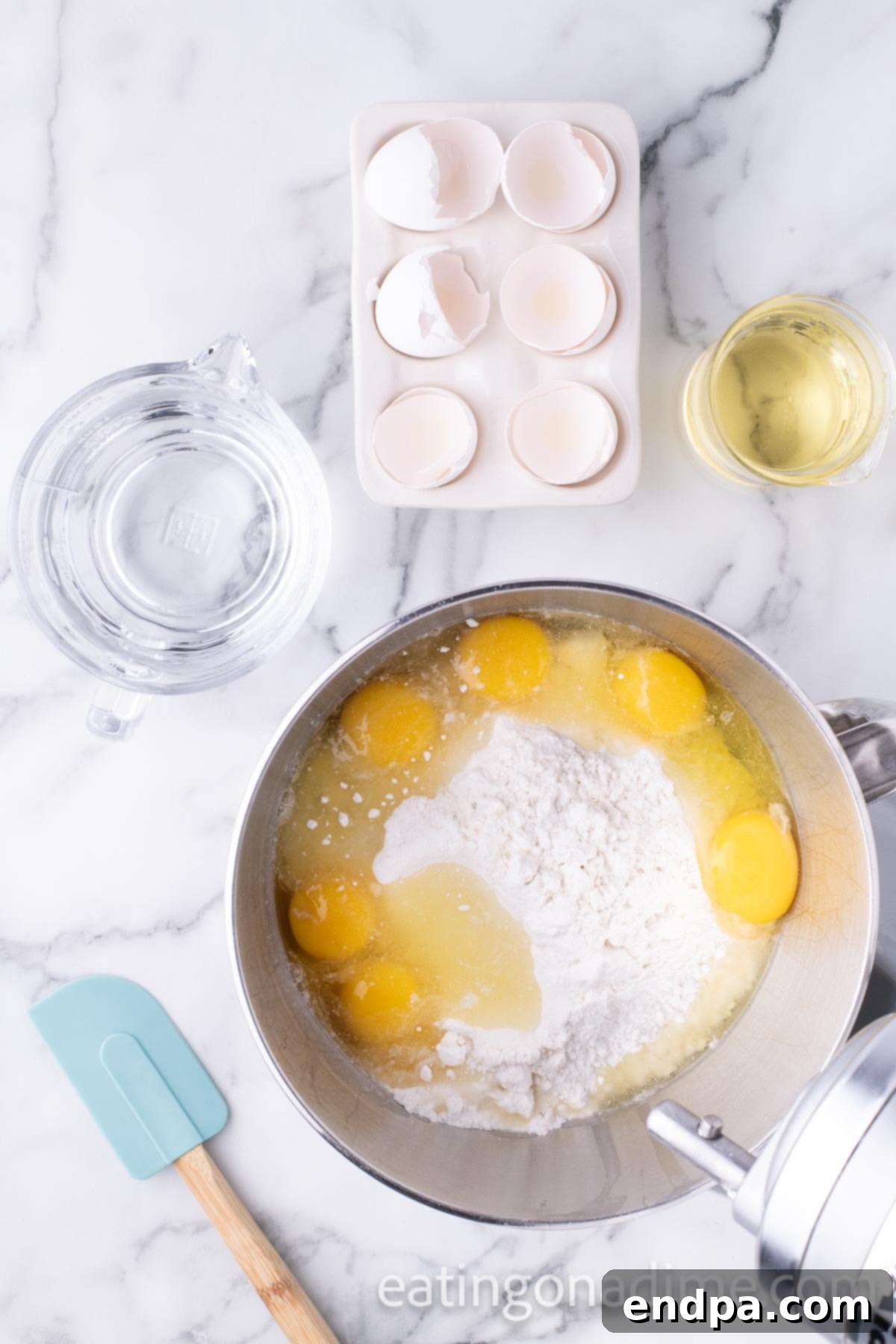 Kaleidoscope Delight 4 Ingredients for cake batter: two boxes of white cake mix, water, vegetable oil, and six large eggs in a large mixing bowl, ready to be combined into a smooth mixture.