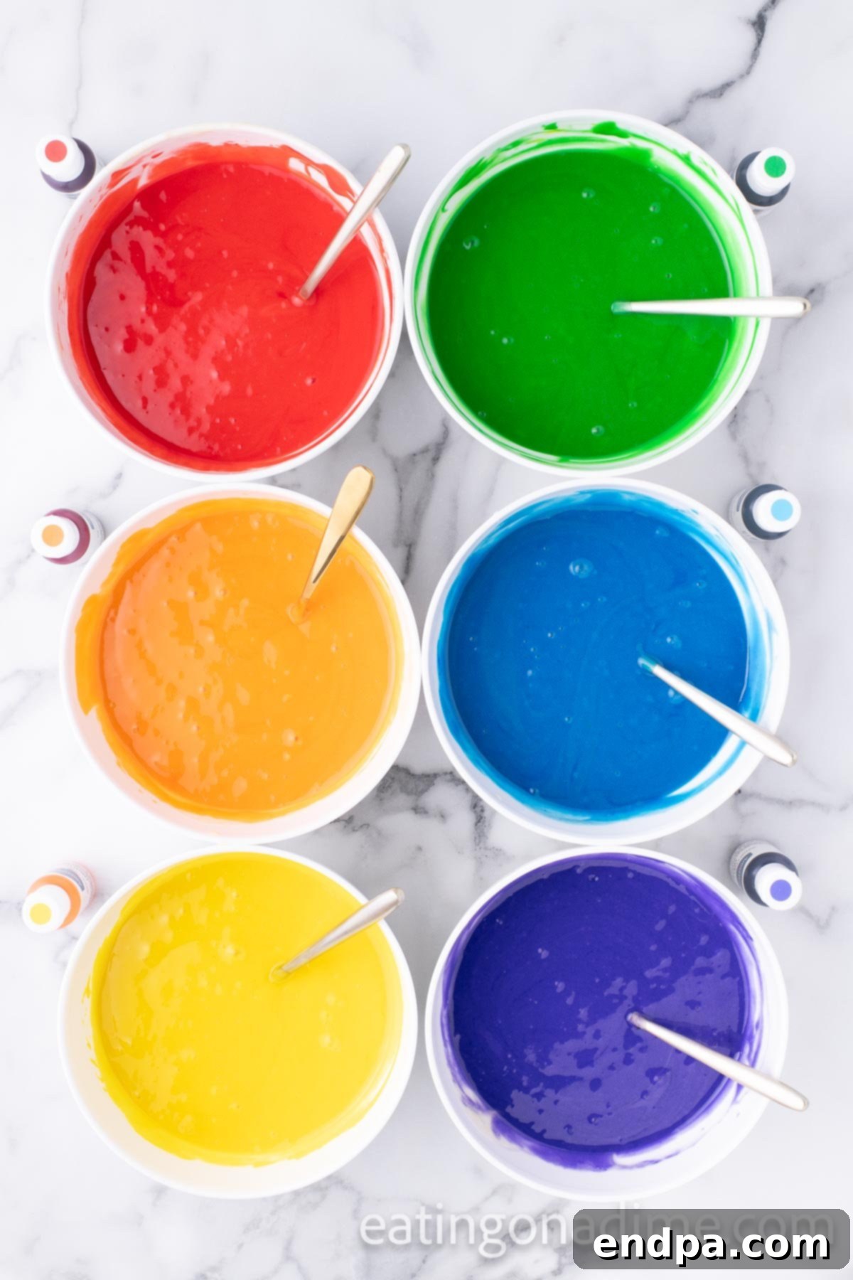 Kaleidoscope Delight 5 Six separate bowls of white cake batter, each dyed a different vibrant color of the rainbow (red, orange, yellow, green, blue, purple) with gel food coloring, showcasing the bright hues before baking.
