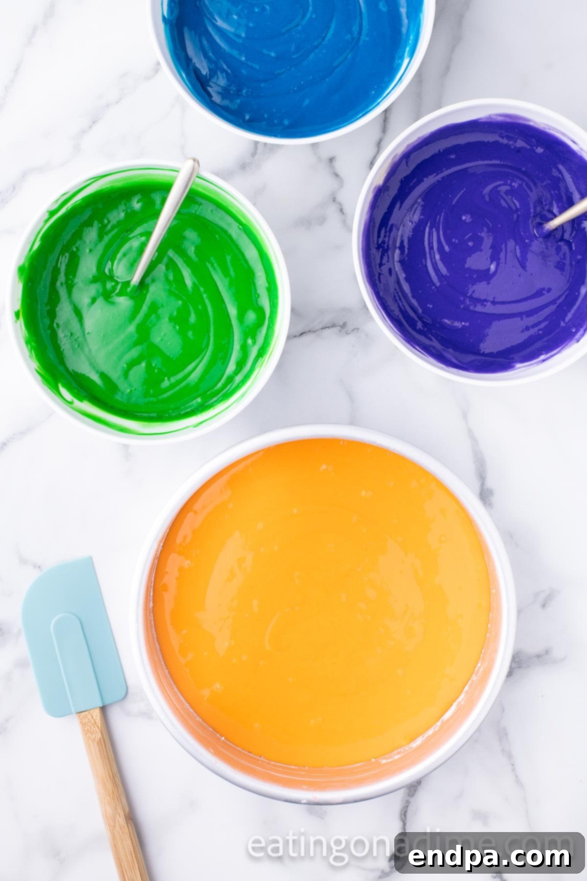 Kaleidoscope Delight 6 Vibrantly colored cake batter, already portioned into three separate round cake pans, demonstrating the even distribution of colors before baking. Additional bowls of colored batter are visible in the background.