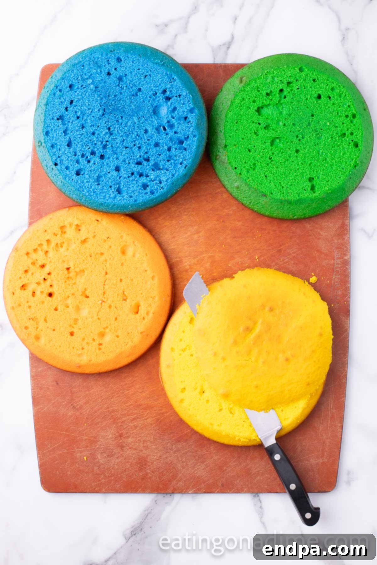 Kaleidoscope Delight 7 Baked cake layers resting on a wire rack, with one layer being leveled carefully with a serrated knife to ensure a flat, even surface for stacking.