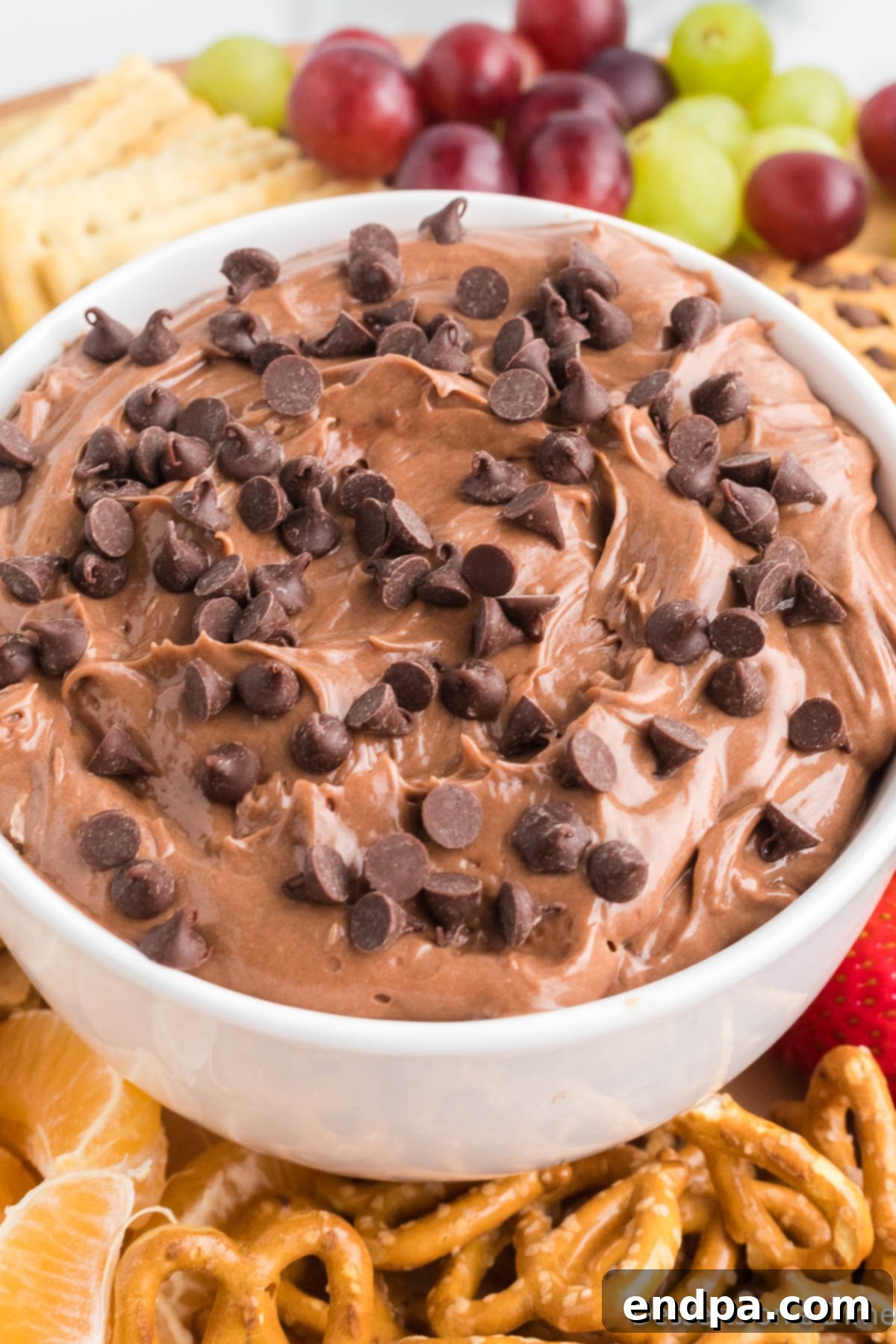Close up image of creamy Nutella dip with fresh strawberries, banana slices, and pretzels ready for dipping