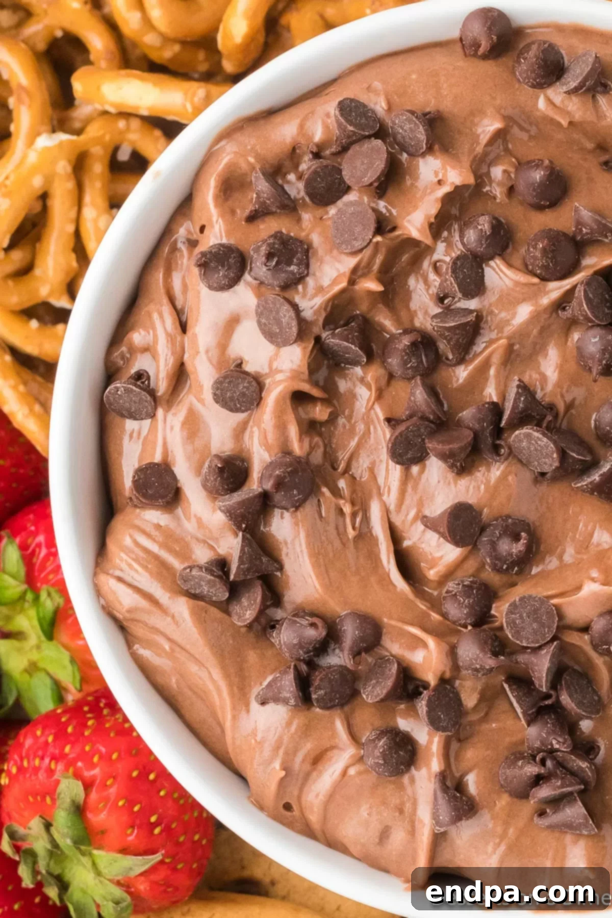 Close up image of Nutella dip in a bowl, with fresh strawberries and pretzels around it