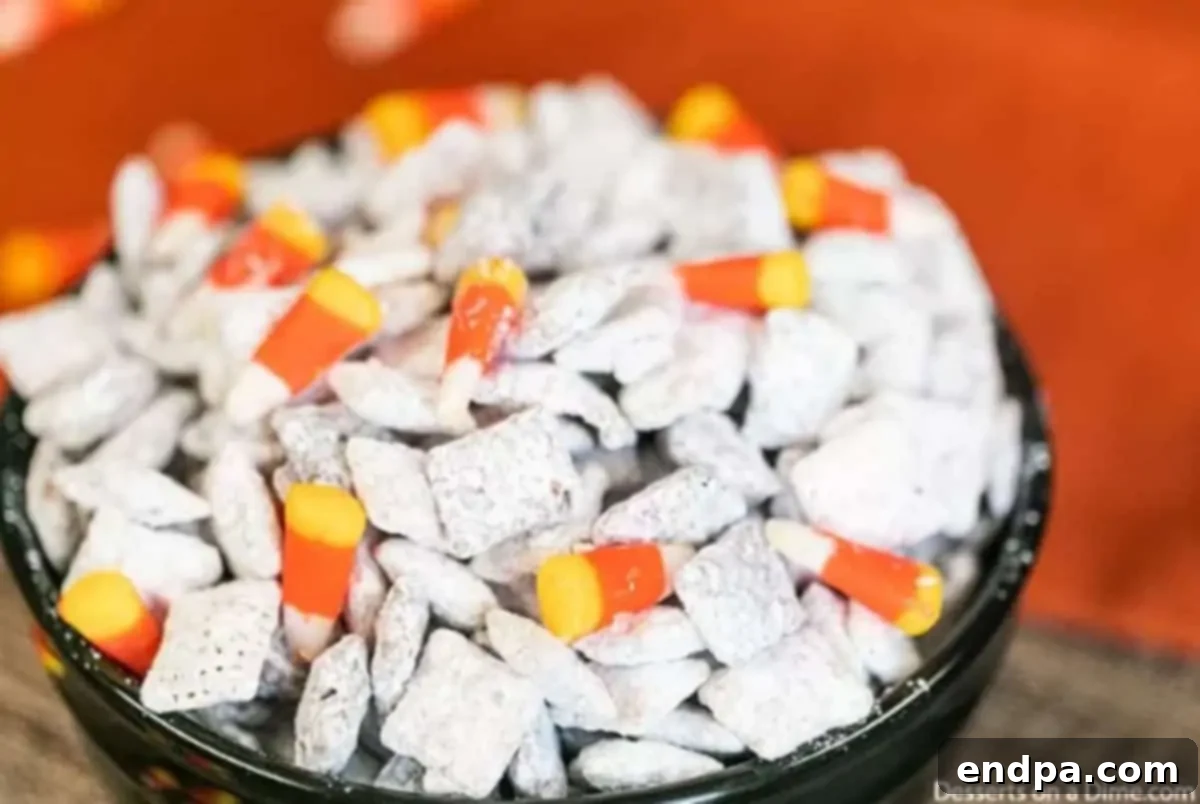 Bowl of festive Halloween Puppy Chow decorated with candy corn and candy eyeballs, ready to serve at a spooky party.