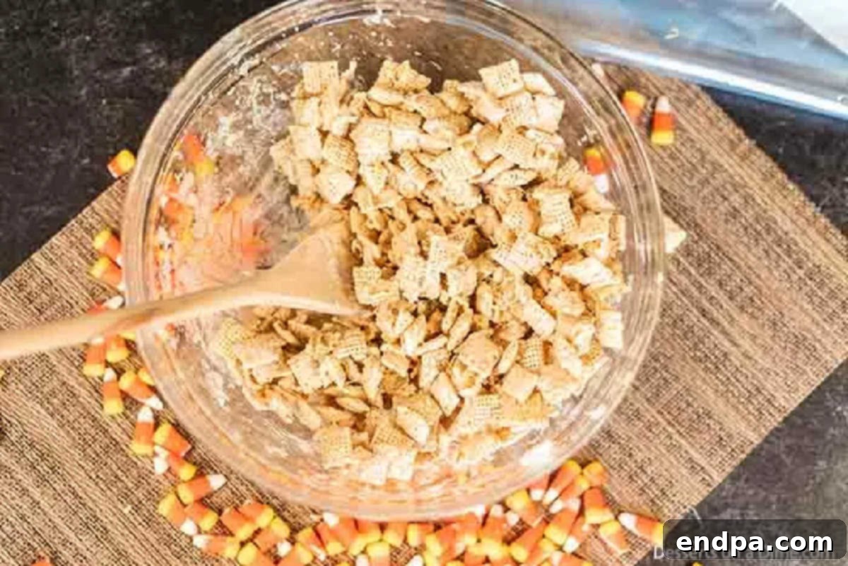 Chex cereal being coated with the melted chocolate and peanut butter mixture in a large bowl, stirred with a spatula.