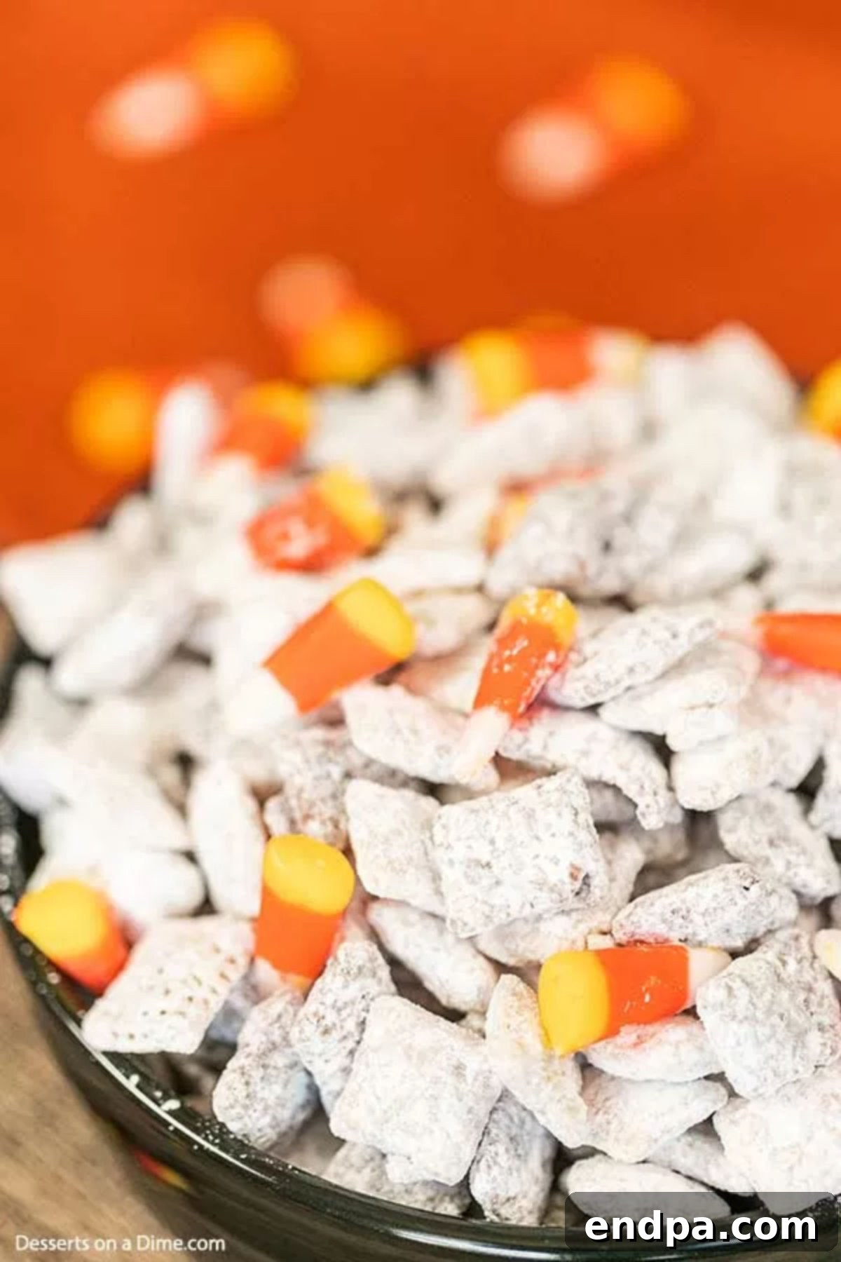 A close-up shot of Halloween Puppy Chow in a black bowl, highlighting the candy corn, candy eyeballs, and chocolate-peanut butter coating.