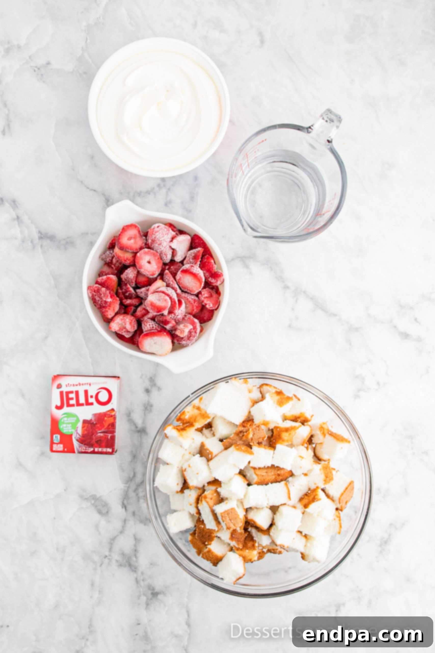 Key ingredients for Strawberry Angel Food Cake laid out: strawberry jell-o mix, a bag of frozen sliced strawberries, a whole angel food cake, and a tub of cool whip.