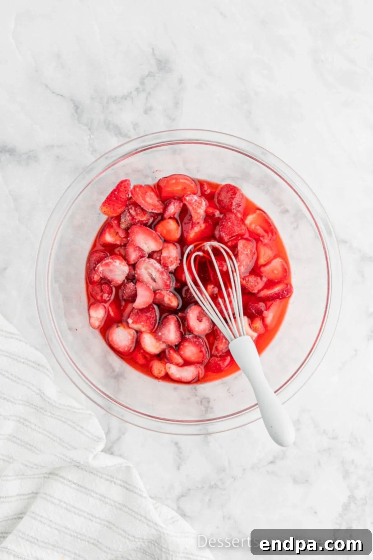 Strawberry Jell-O powder mixed with boiling water and frozen strawberries in a glass bowl, starting to set.