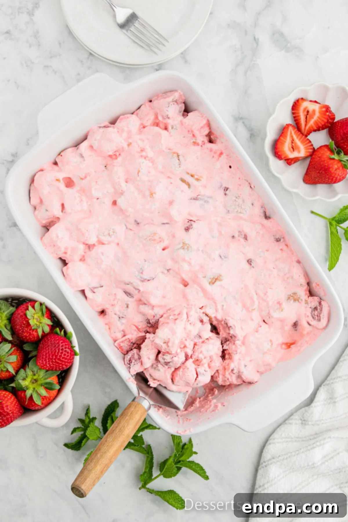 A slice of Strawberry Angel Food Cake being lifted from the baking dish, revealing its creamy layers and a fresh strawberry garnish.