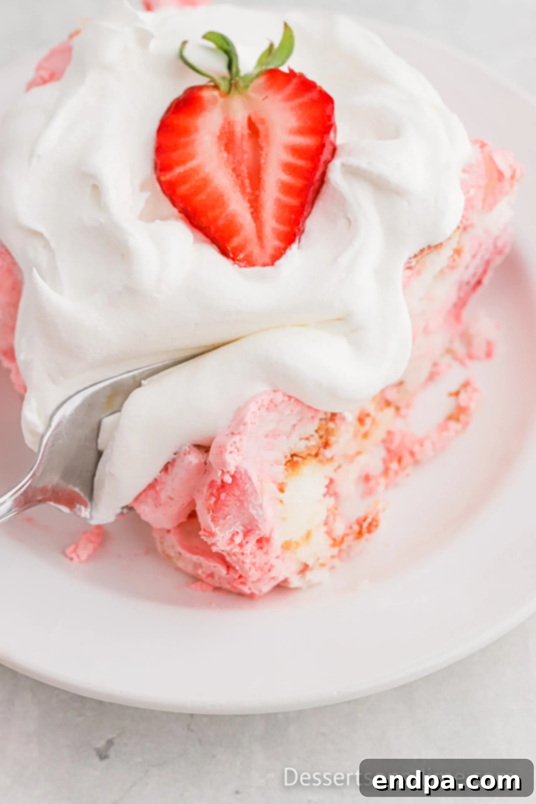 A close-up shot of a slice of Strawberry Angel Food Cake on a plate, garnished with fresh mint and a whole strawberry, highlighting its light texture.