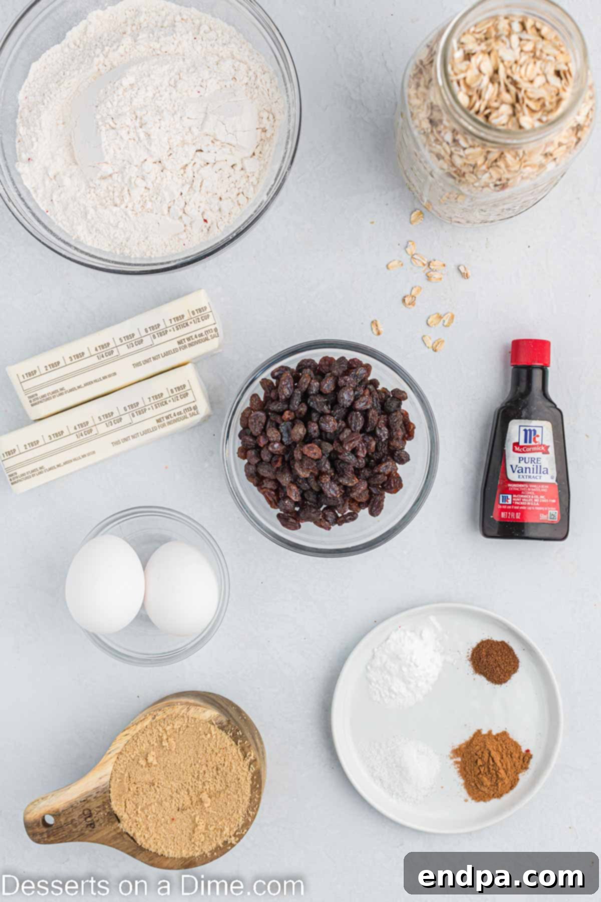 This is the best recipe for soft and chewy Oatmeal raisin cookies. They are so decadent and everyone will think you bought them at a bakery. Make these moist homemade cookies today for an easy treat. A collection of essential ingredients for baking oatmeal raisin cookies, including butter, brown sugar, eggs, flour, baking soda, salt, cinnamon, cloves, vanilla, rolled oats, and raisins, artfully arranged on a rustic wooden surface.