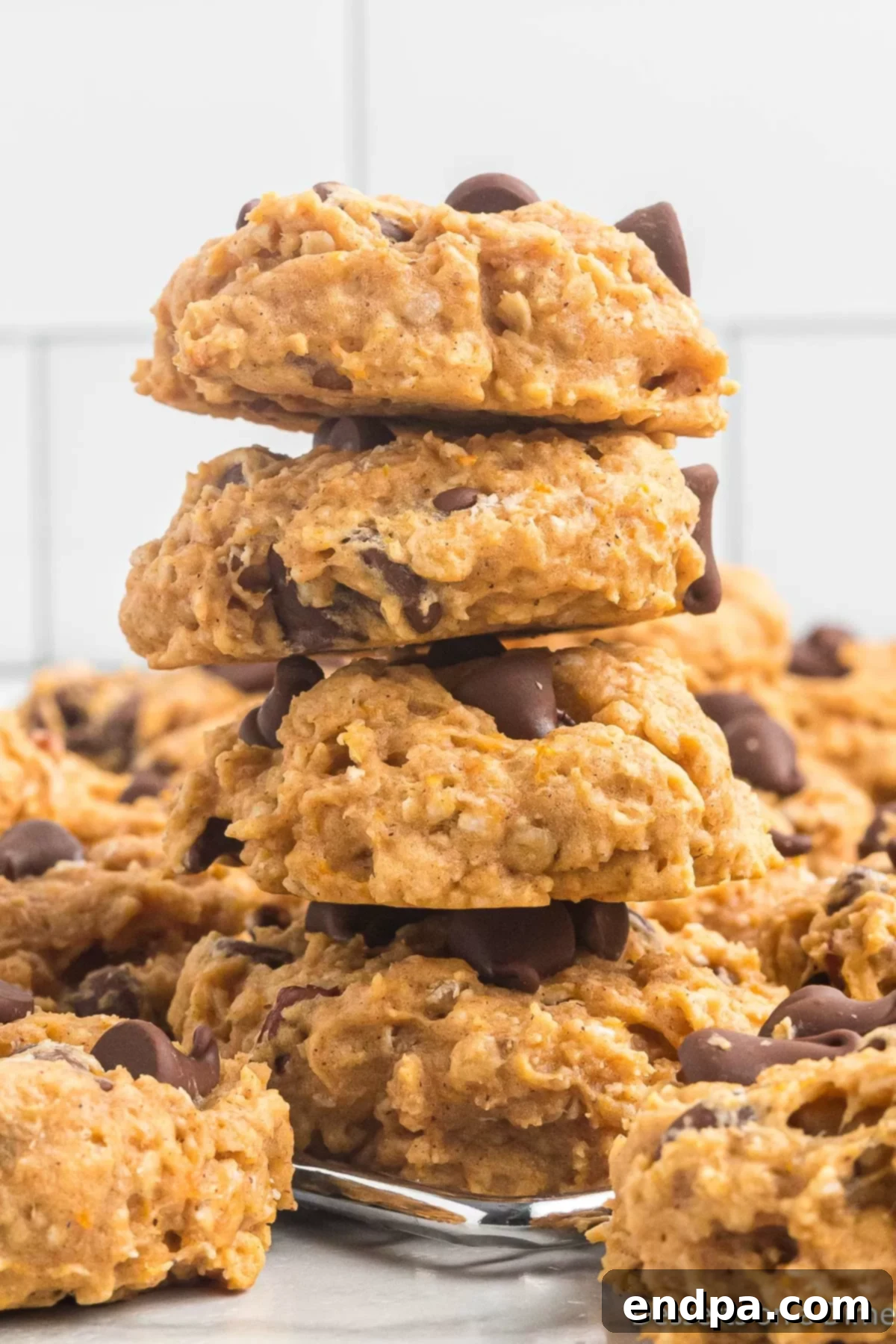 Golden Sweet Potato Cookies 2 A stack of golden brown sweet potato cookies, garnished with chocolate chips and chopped pecans, resting on a cooling rack.