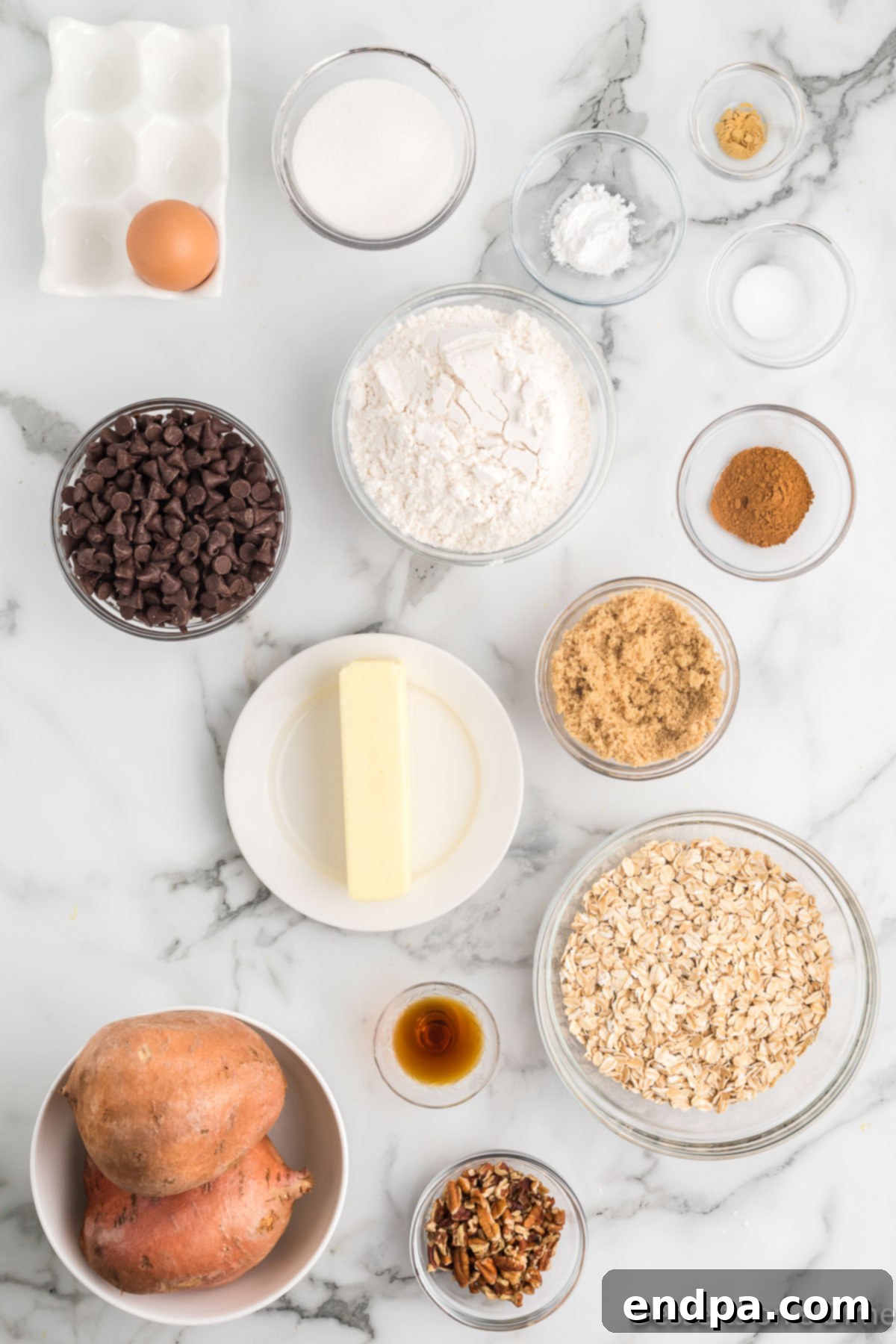 Golden Sweet Potato Cookies 3 A flat lay photograph showcasing all the raw ingredients needed for sweet potato cookies: sweet potatoes, bags of flour, oats, baking powder, butter, brown sugar, granulated sugar, chocolate chips, and pecans.