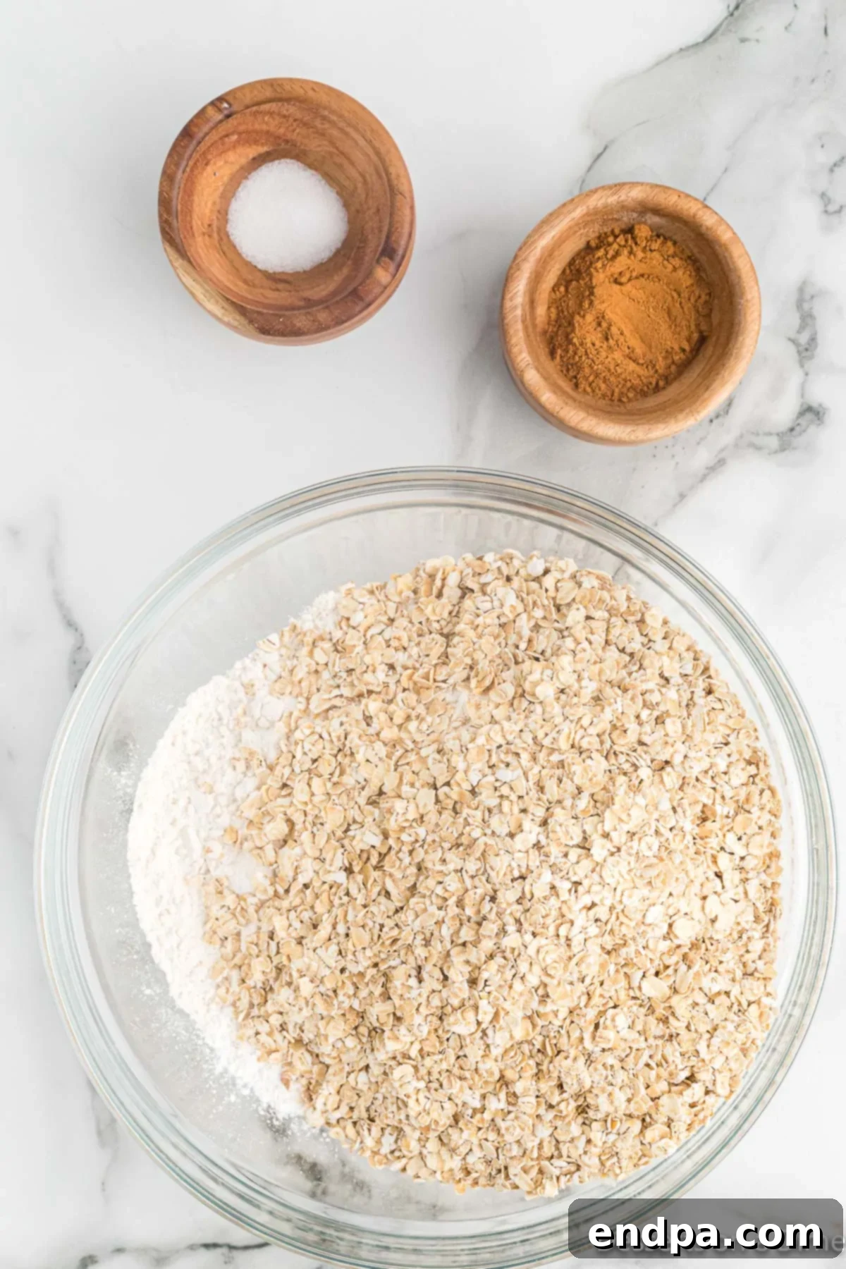 Golden Sweet Potato Cookies 5 Rolled oats and ground cinnamon being added to the flour and baking powder mixture in a bowl.