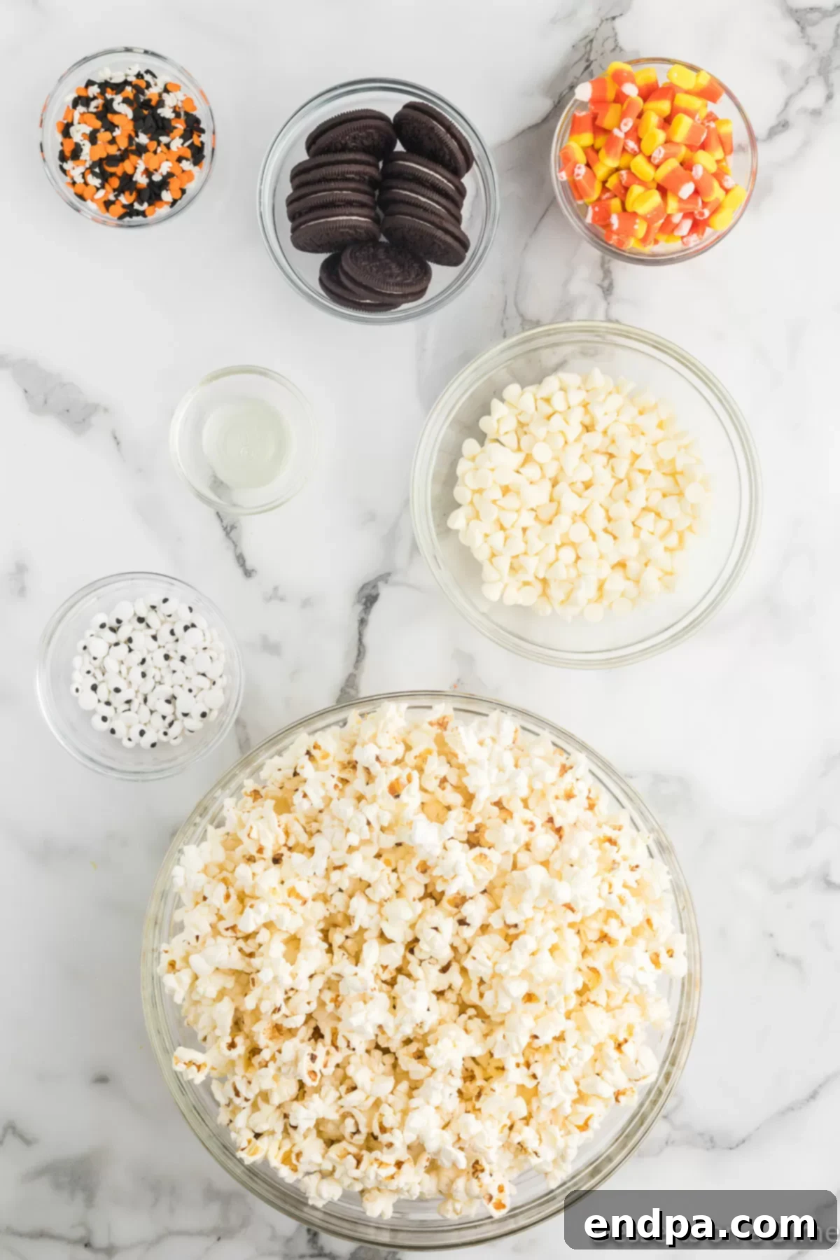Haunted Kernels 3 Individual ingredients laid out for Halloween Popcorn including popped popcorn, white chocolate chips, vegetable oil, Oreo cookies, candy corn, and Halloween sprinkles.