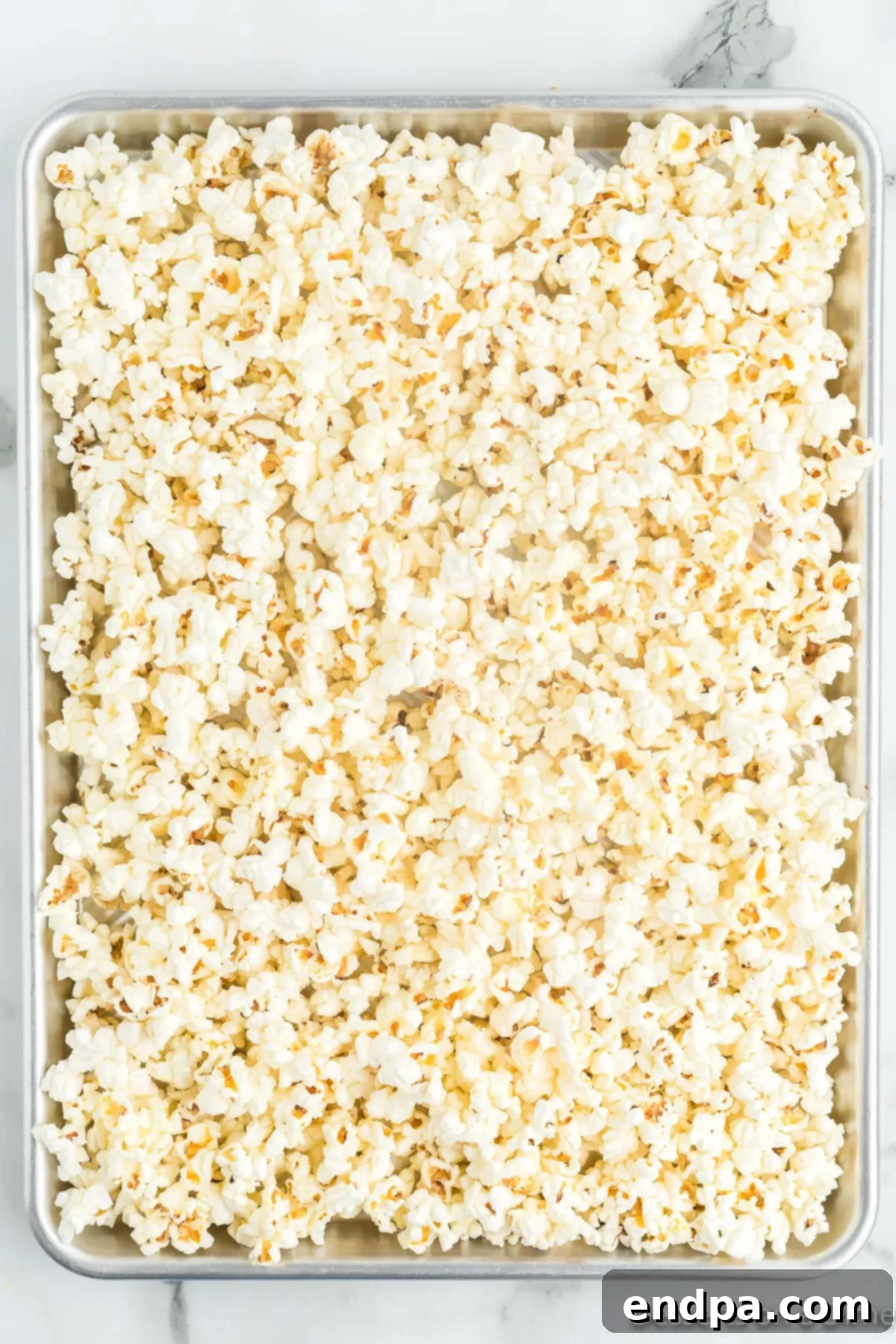 Haunted Kernels 4 Popped popcorn spread out evenly on a baking sheet, ready for toppings.