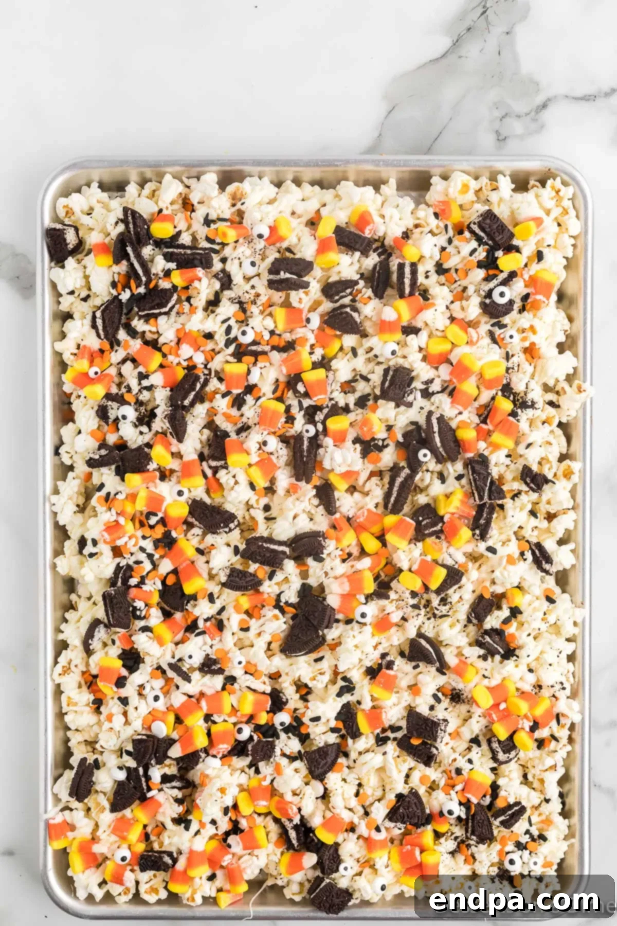 Haunted Kernels 7 A close-up of popcorn covered in white chocolate, being topped with crushed Oreo cookies, candy corn, and whimsical candy eyes.
